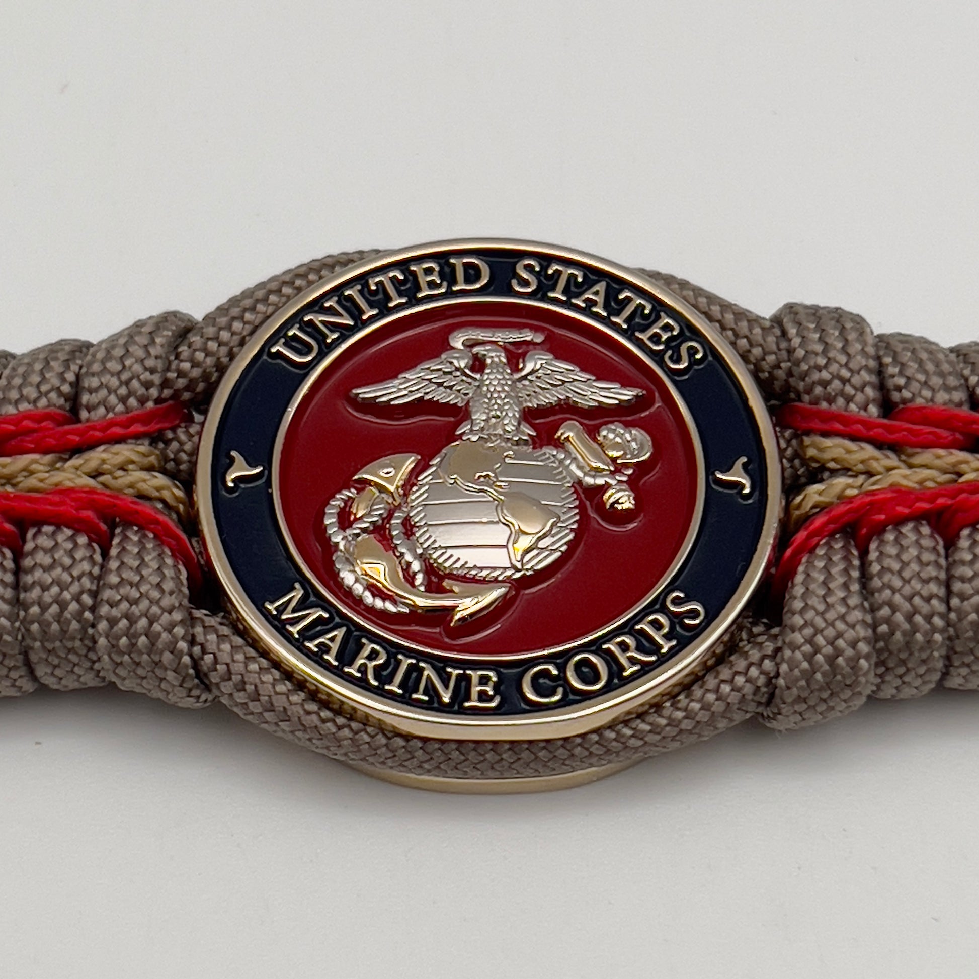 Thick and comfortable braided United States Marine Corps bracelet featuring a 24K gold and silver plated USMC officer Eagle Globe and Anchor medallion, a Cobra style tactical buckle and woven with tan 550, Imperial red and gold micro paracord.
