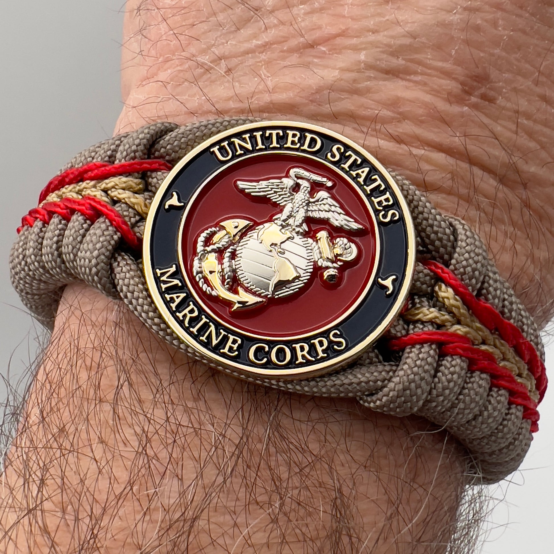 Thick and comfortable braided United States Marine Corps bracelet featuring a 24K gold and silver plated USMC officer Eagle Globe and Anchor medallion, a Cobra style tactical buckle and woven with tan 550, Imperial red and gold micro paracord.