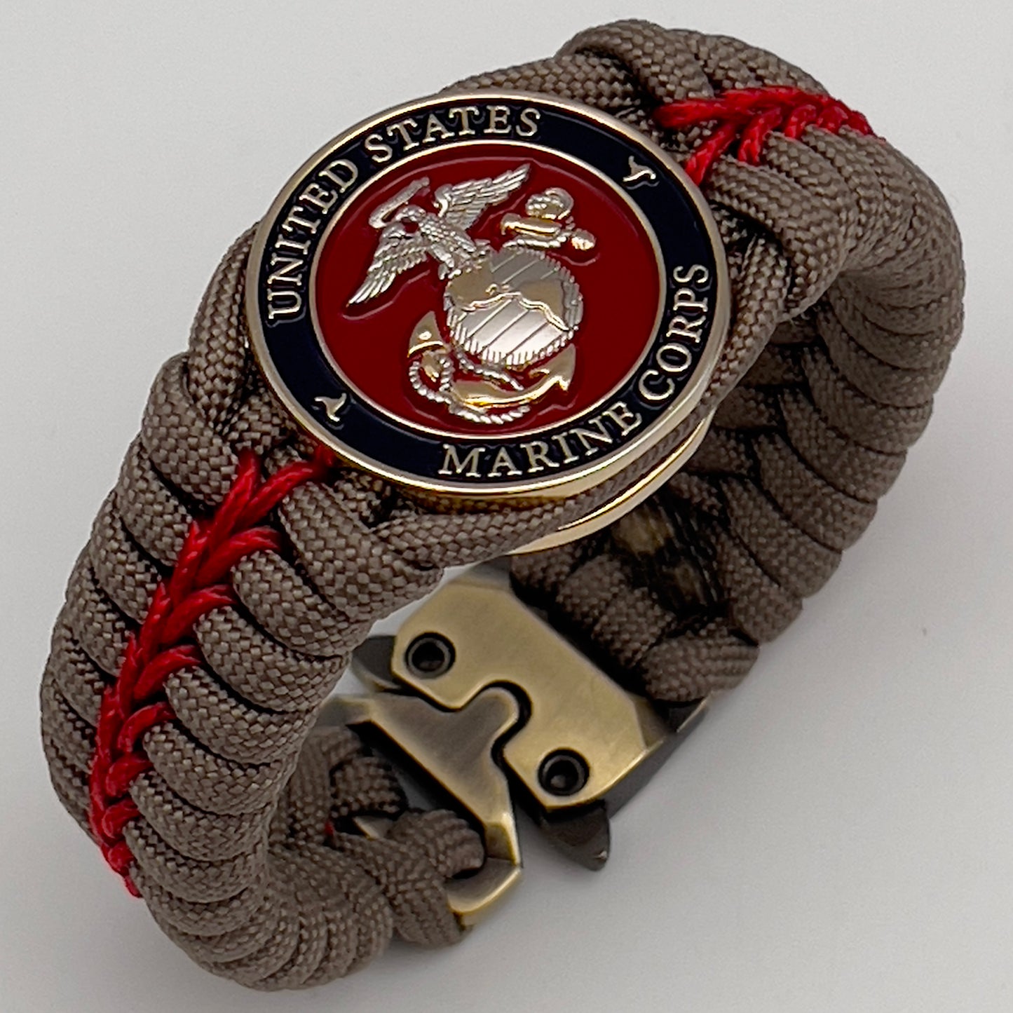 Thick, semi-rigid and comfortable braided United States Marine Corps bracelet featuring a 24K gold and silver plated USMC officer Eagle Globe and Anchor medallion, a gold Cobra style tactical buckle and woven with tan 550 paracord and Imperial red micro cord.