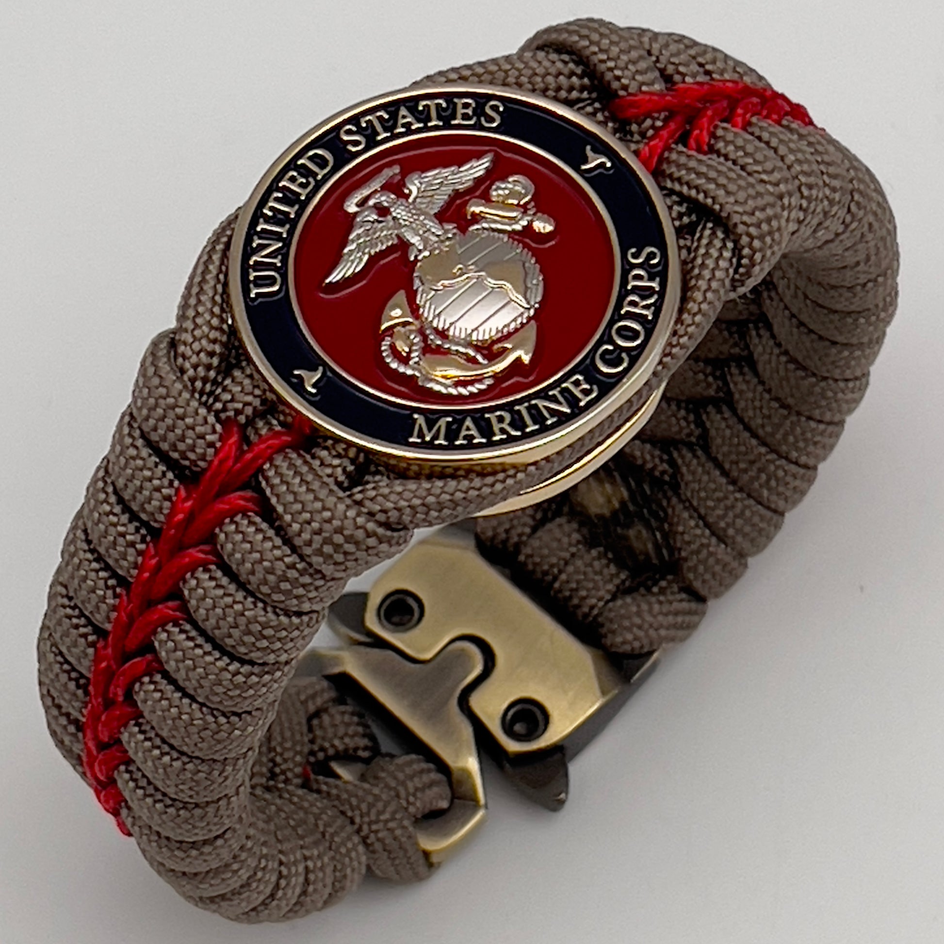Thick, semi-rigid and comfortable braided United States Marine Corps bracelet featuring a 24K gold and silver plated USMC officer Eagle Globe and Anchor medallion, a gold Cobra style tactical buckle and woven with tan 550 paracord and Imperial red micro cord.