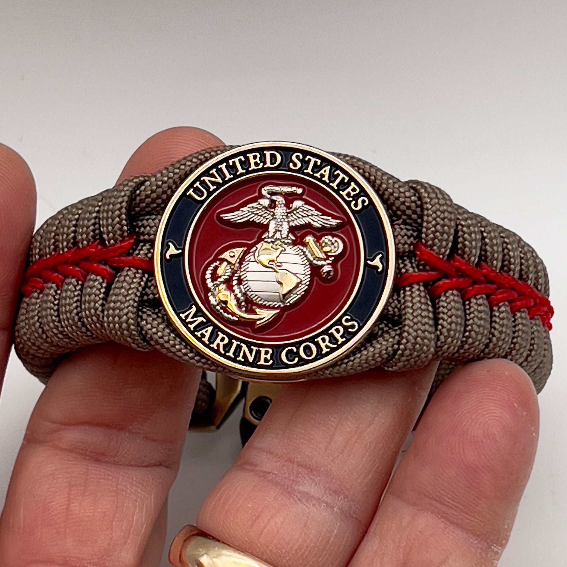 Thick, semi-rigid and comfortable braided United States Marine Corps bracelet featuring a 24K gold and silver plated USMC officer Eagle Globe and Anchor medallion, a gold Cobra style tactical buckle and woven with tan 550 paracord and Imperial red micro cord.