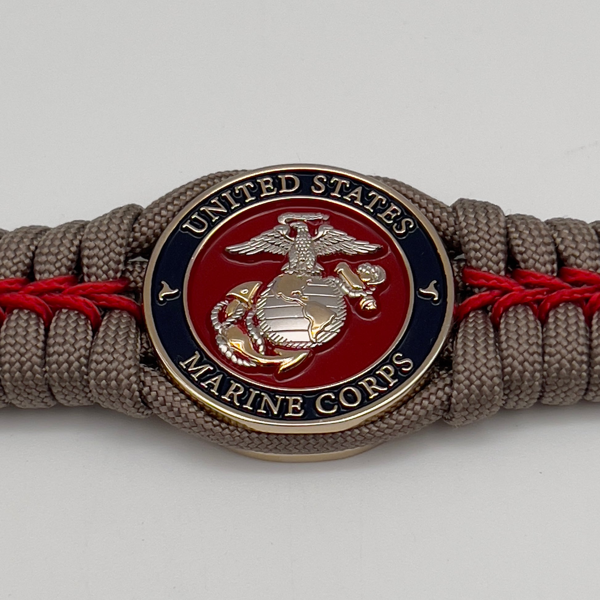 Thick, semi-rigid and comfortable braided United States Marine Corps bracelet featuring a 24K gold and silver plated USMC officer Eagle Globe and Anchor medallion, a gold Cobra style tactical buckle and woven with tan 550 paracord and Imperial red micro cord.