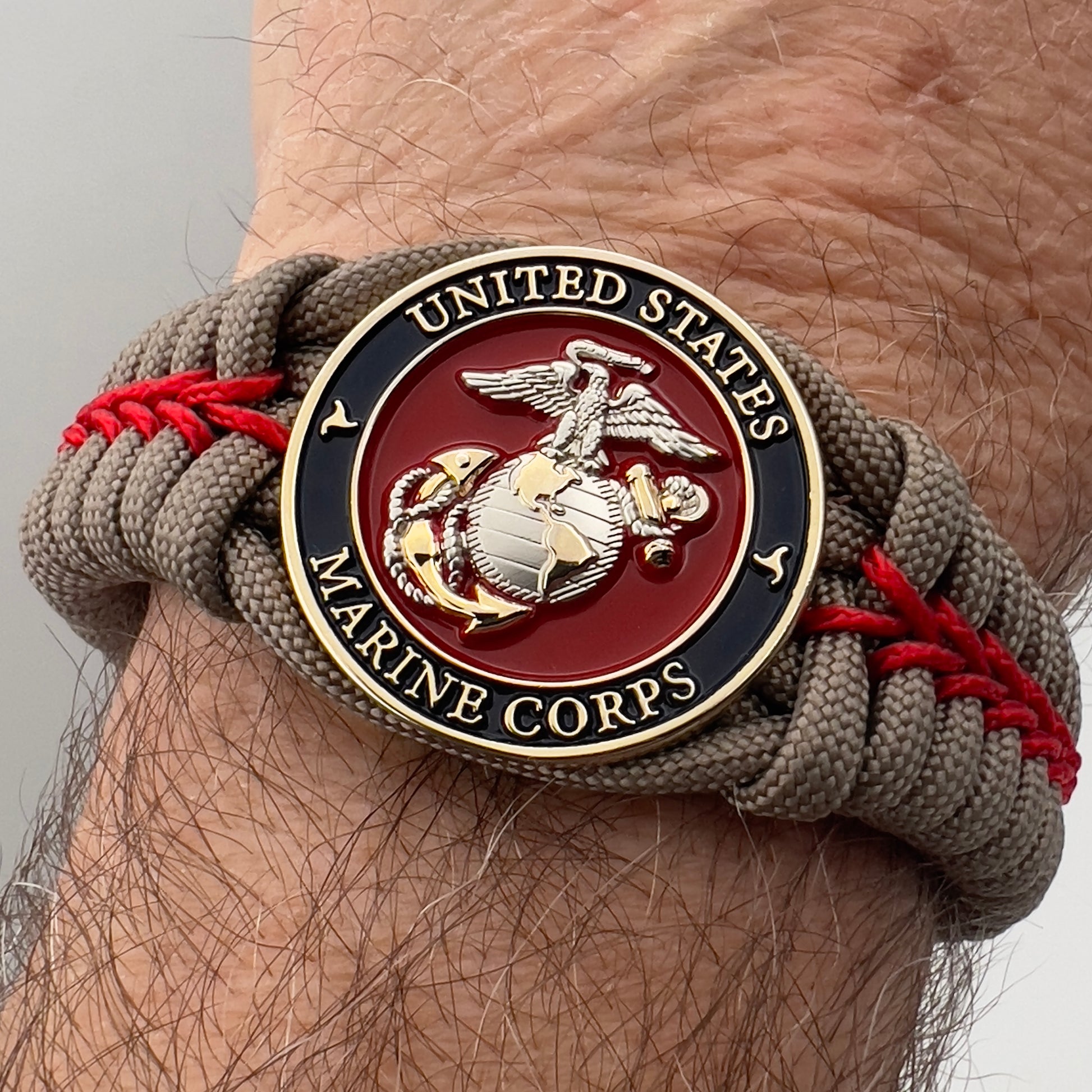 Thick, semi-rigid and comfortable braided United States Marine Corps bracelet featuring a 24K gold and silver plated USMC officer Eagle Globe and Anchor medallion, a gold Cobra style tactical buckle and woven with tan 550 paracord and Imperial red micro cord.
