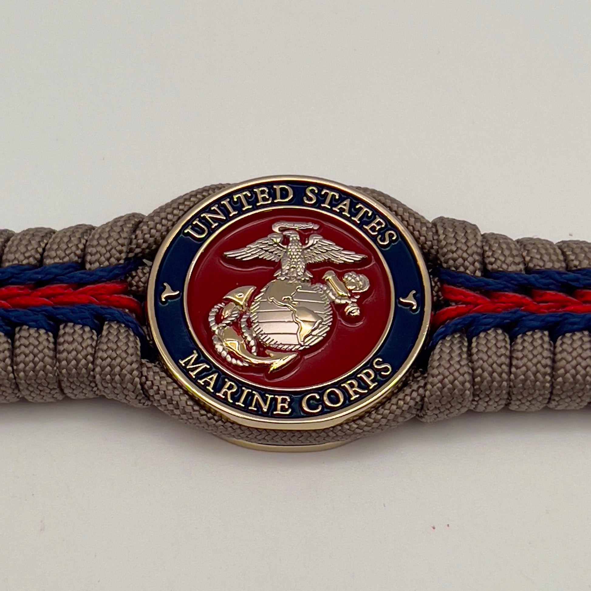 Thick, semi-rigid and comfortable braided United States Marine Corps bracelet featuring a 24K gold and silver plated USMC officer Eagle Globe and Anchor medallion, a gold Cobra style tactical buckle and woven with tan 550 paracord and Imperial red and gold micro cord.