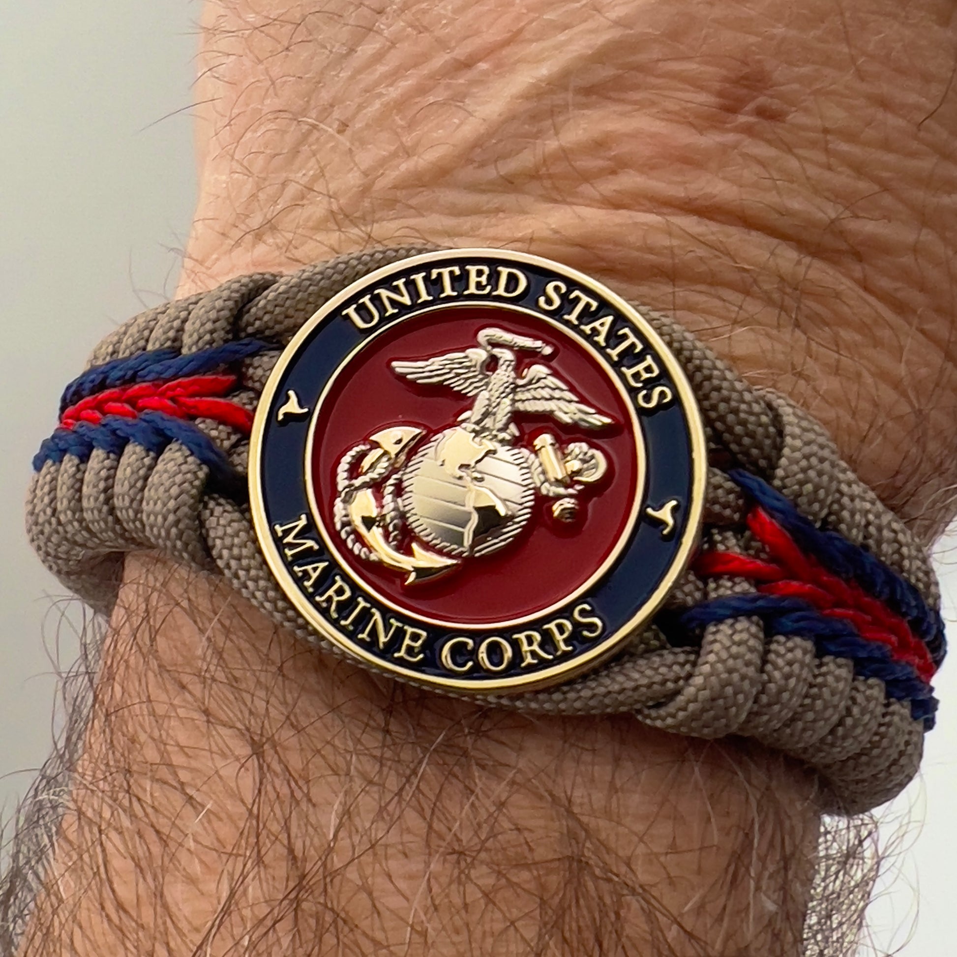 Thick, semi-rigid and comfortable braided United States Marine Corps bracelet featuring a 24K gold and silver plated USMC officer Eagle Globe and Anchor medallion, a gold Cobra style tactical buckle and woven with tan 550 paracord and Imperial red and gold micro cord.