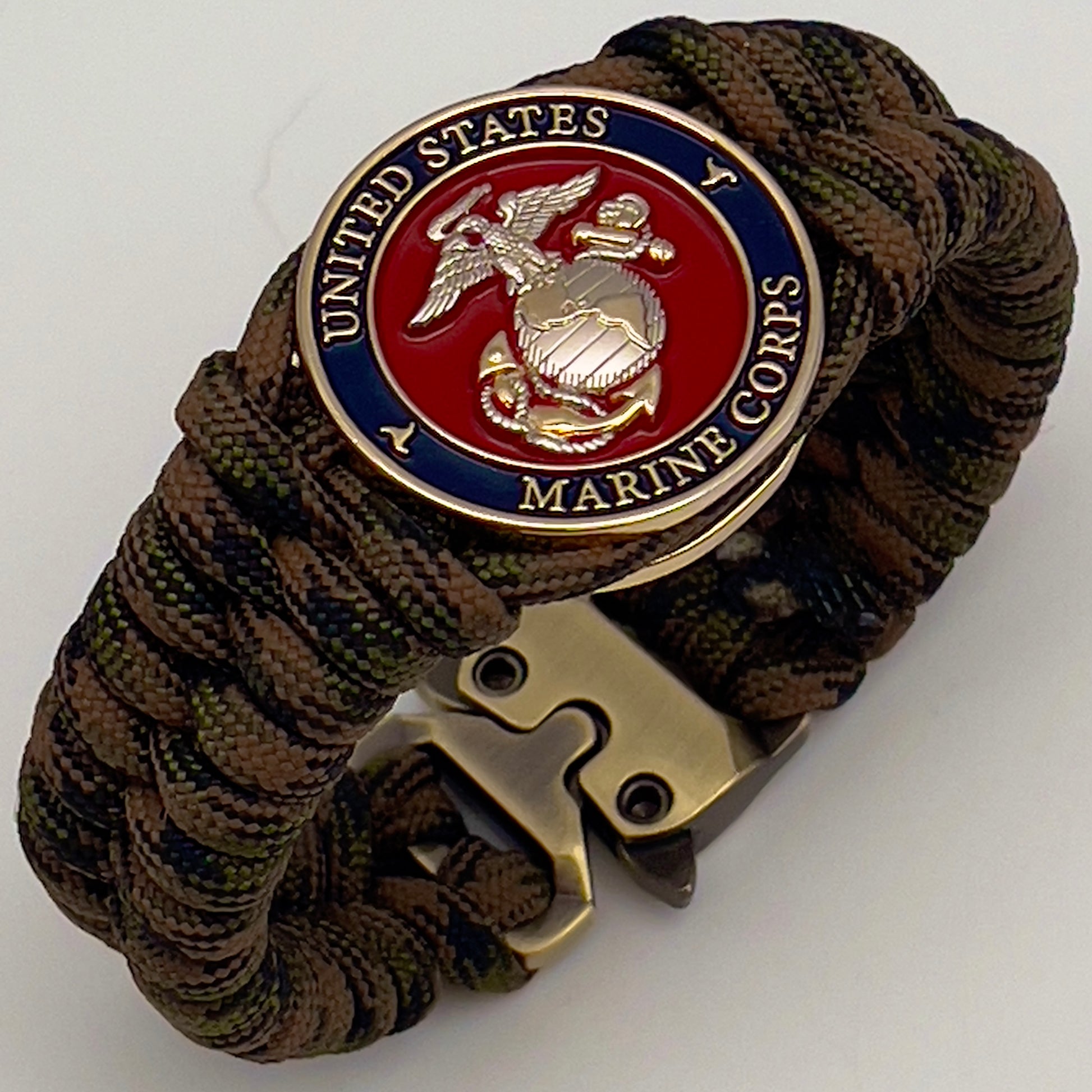 Thick, semi-rigid and comfortable braided United States Marine Corps bracelet featuring a 24K gold and silver plated USMC officer Eagle Globe and Anchor medallion, a gold Cobra style tactical buckle and woven with Woodland Camo 550 paracord.