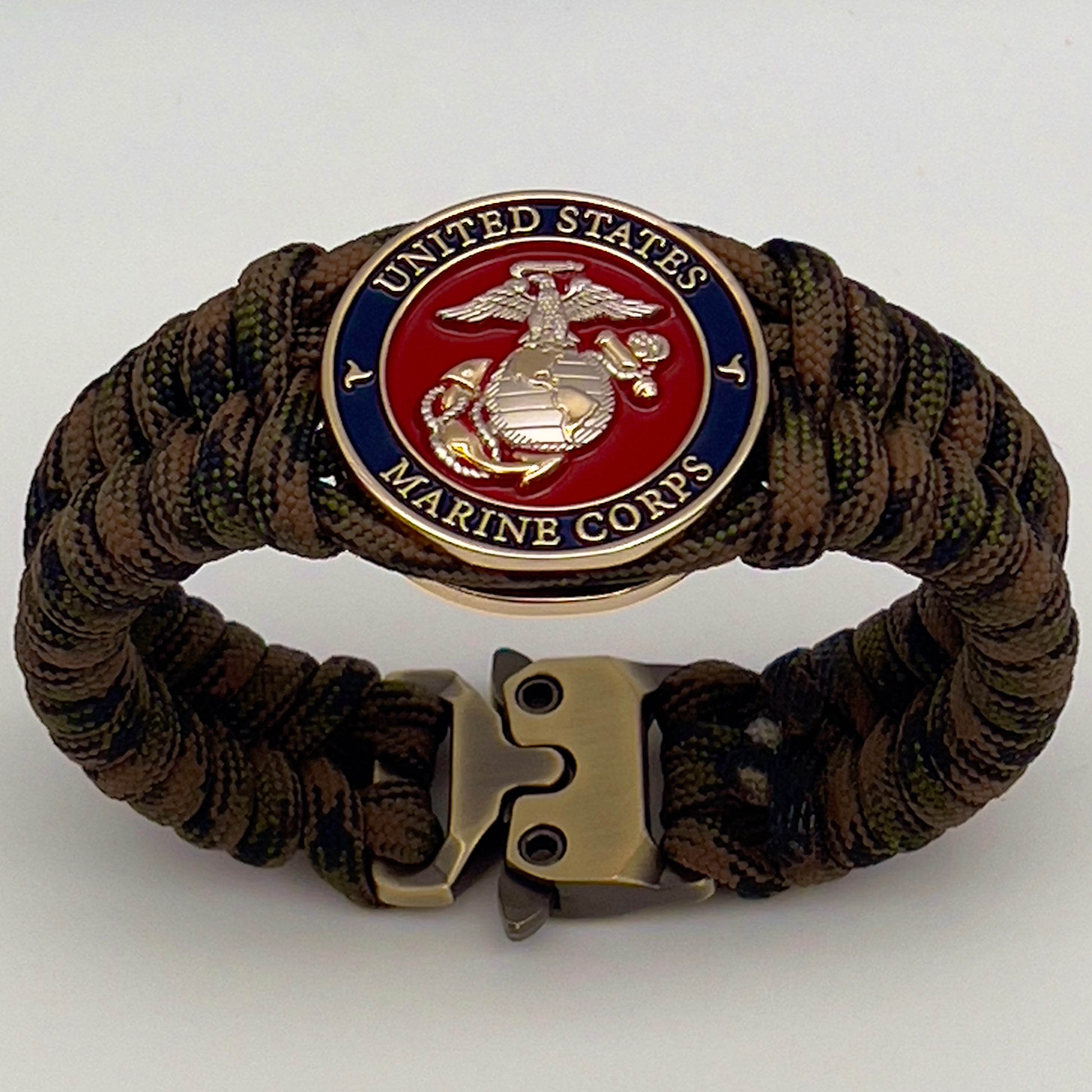 Thick, semi-rigid and comfortable braided United States Marine Corps bracelet featuring a 24K gold and silver plated USMC officer Eagle Globe and Anchor medallion, a gold Cobra style tactical buckle and woven with Woodland Camo 550 paracord.