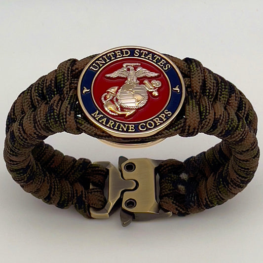 Thick, semi-rigid and comfortable braided United States Marine Corps bracelet featuring a 24K gold and silver plated USMC officer Eagle Globe and Anchor medallion, a gold Cobra style tactical buckle and woven with Woodland Camo 550 paracord.
