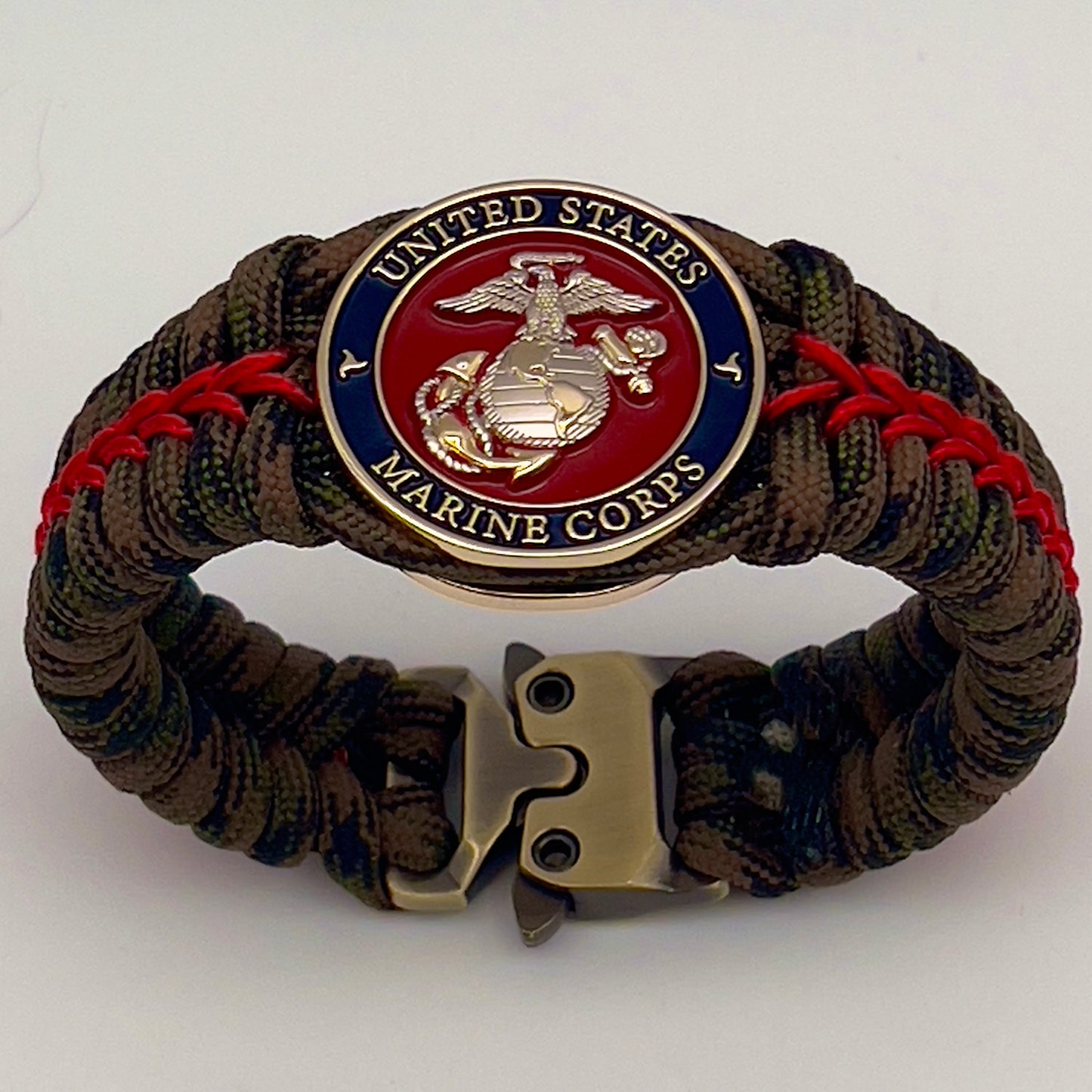 Thick, semi-rigid and comfortable braided United States Marine Corps bracelet featuring a 24K gold and silver plated USMC officer Eagle Globe and Anchor medallion, a gold Cobra style tactical buckle and woven with Woodland Camo 550 paracord and Imperial Red micro cord.