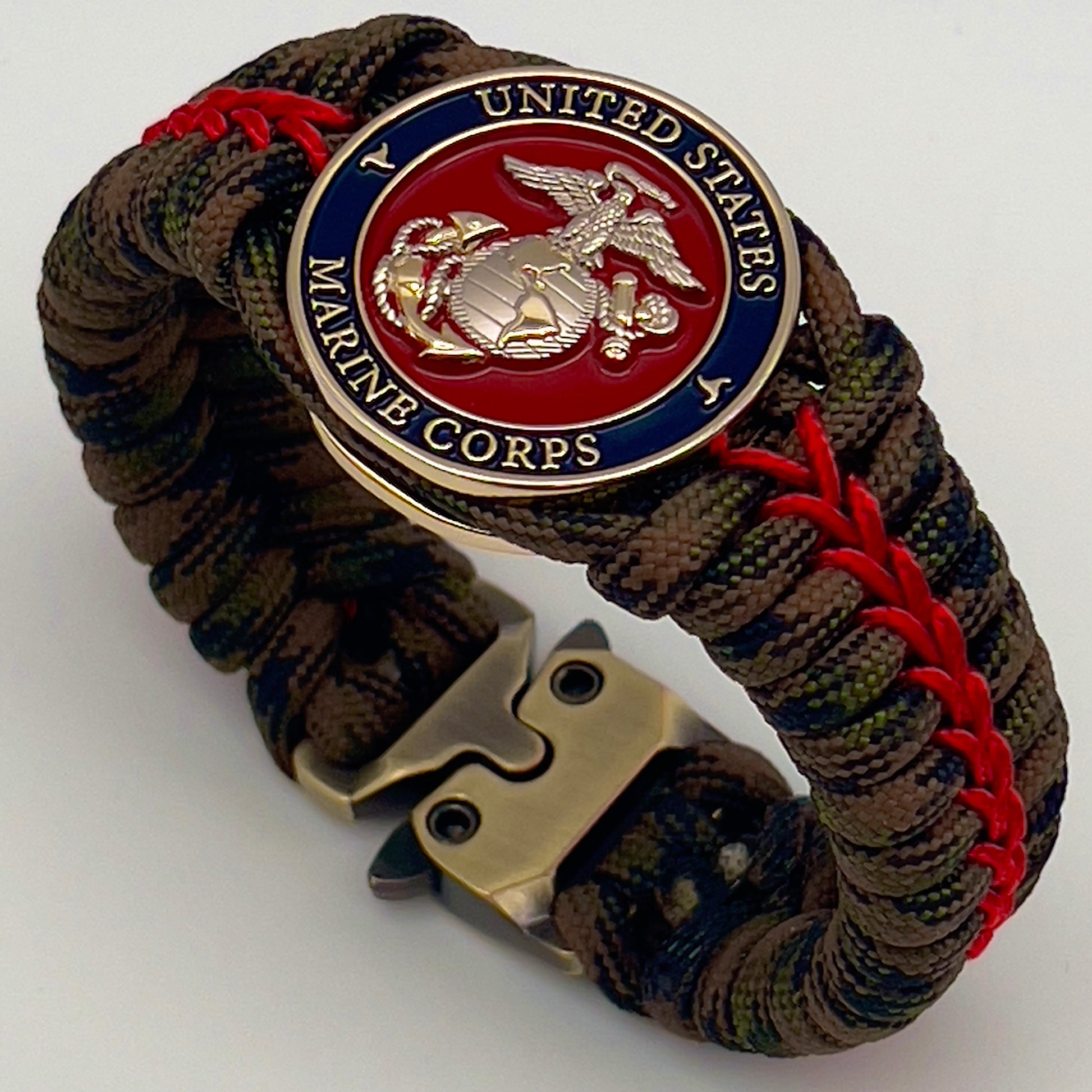 Thick, semi-rigid and comfortable braided United States Marine Corps bracelet featuring a 24K gold and silver plated USMC officer Eagle Globe and Anchor medallion, a gold Cobra style tactical buckle and woven with Woodland Camo 550 paracord and Imperial Red micro cord.