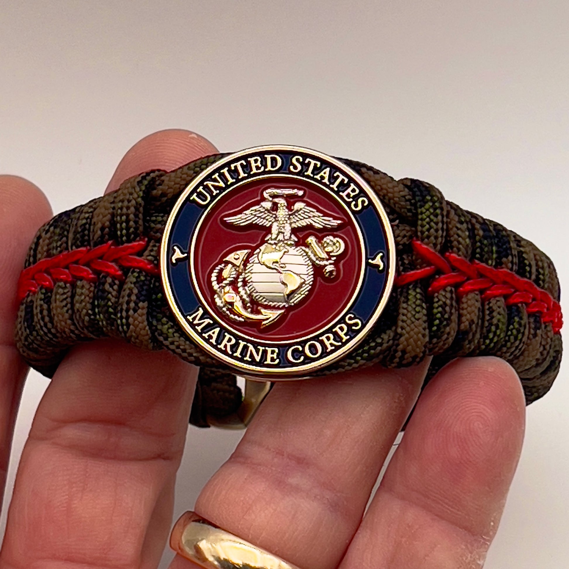 Thick, semi-rigid and comfortable braided United States Marine Corps bracelet featuring a 24K gold and silver plated USMC officer Eagle Globe and Anchor medallion, a gold Cobra style tactical buckle and woven with Woodland Camo 550 paracord and Imperial Red micro cord.