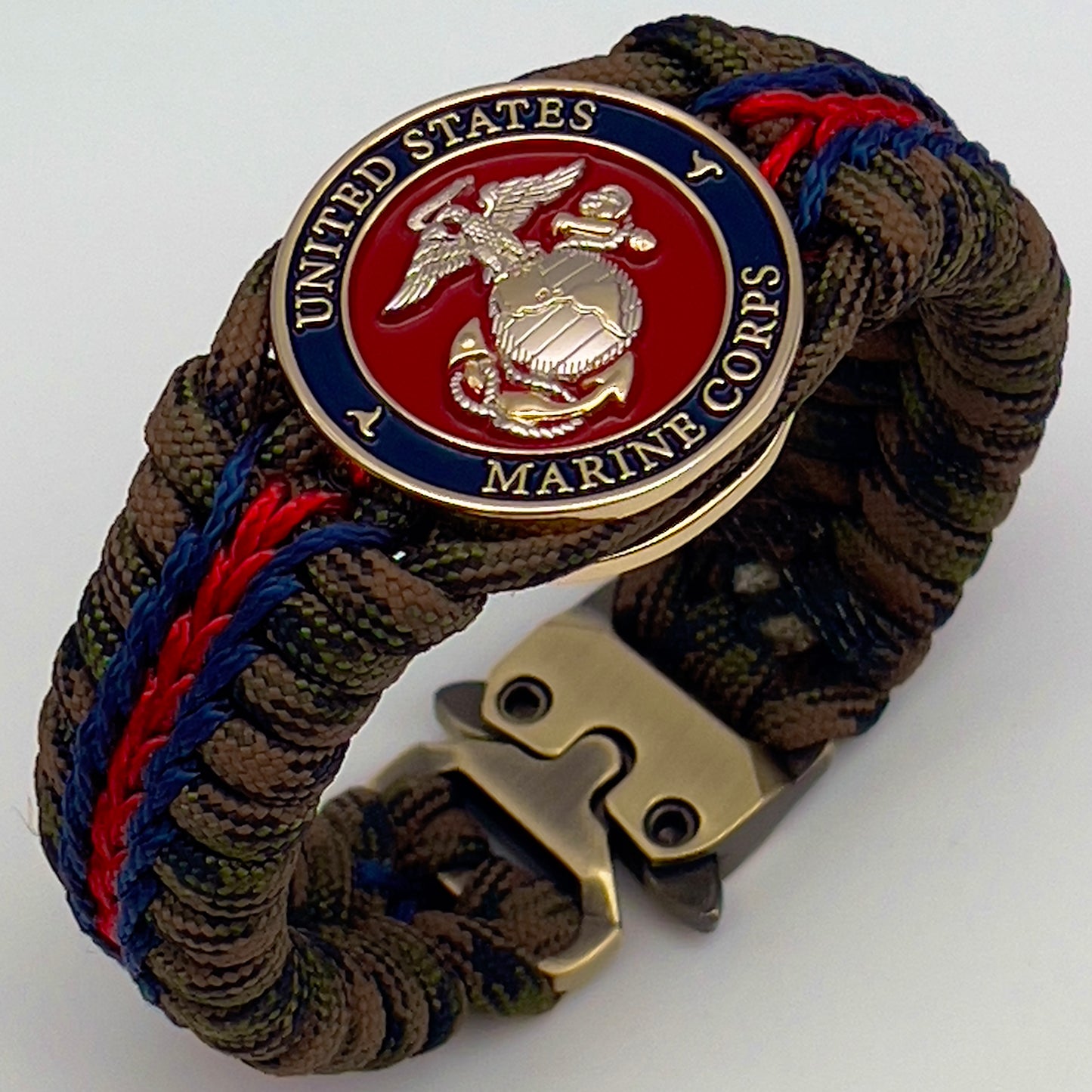 Thick, semi-rigid and comfortable braided United States Marine Corps bracelet featuring a 24K gold and silver plated USMC officer Eagle Globe and Anchor medallion, a gold Cobra style tactical buckle and woven with Woodland Camo 550 paracord and Imperial Red and Navy Blue micro cord.