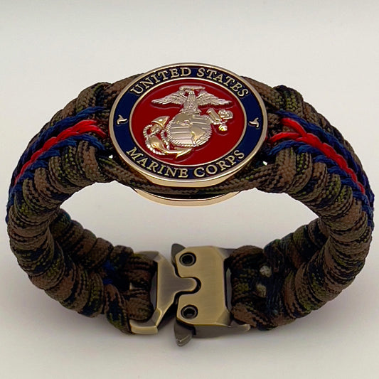 Thick, semi-rigid and comfortable braided United States Marine Corps bracelet featuring a 24K gold and silver plated USMC officer Eagle Globe and Anchor medallion, a gold Cobra style tactical buckle and woven with Woodland Camo 550 paracord and Imperial Red and Navy Blue micro cord.