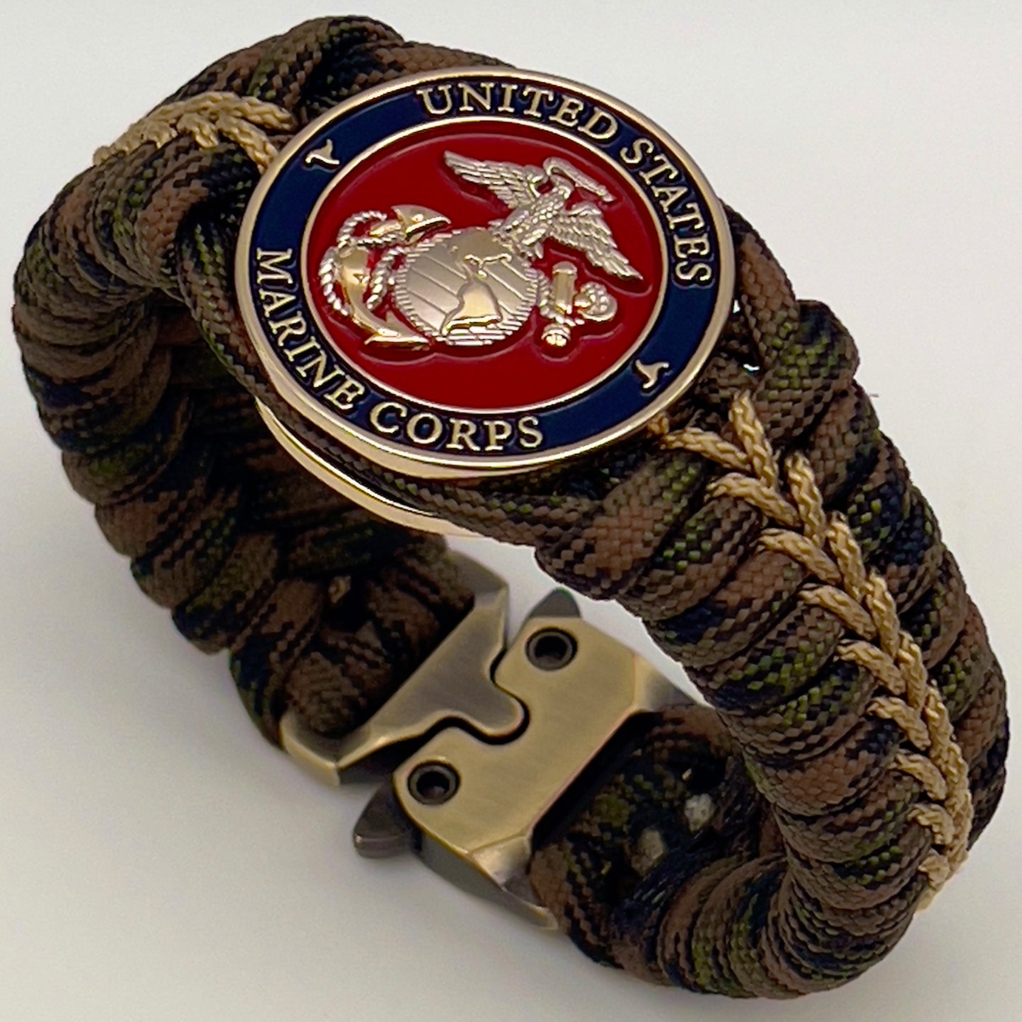 Thick, semi-rigid and comfortable braided United States Marine Corps bracelet featuring a 24K gold and silver plated USMC officer Eagle Globe and Anchor medallion, a gold Cobra style tactical buckle and woven with Woodland Camo 550 paracord and gold micro cord.