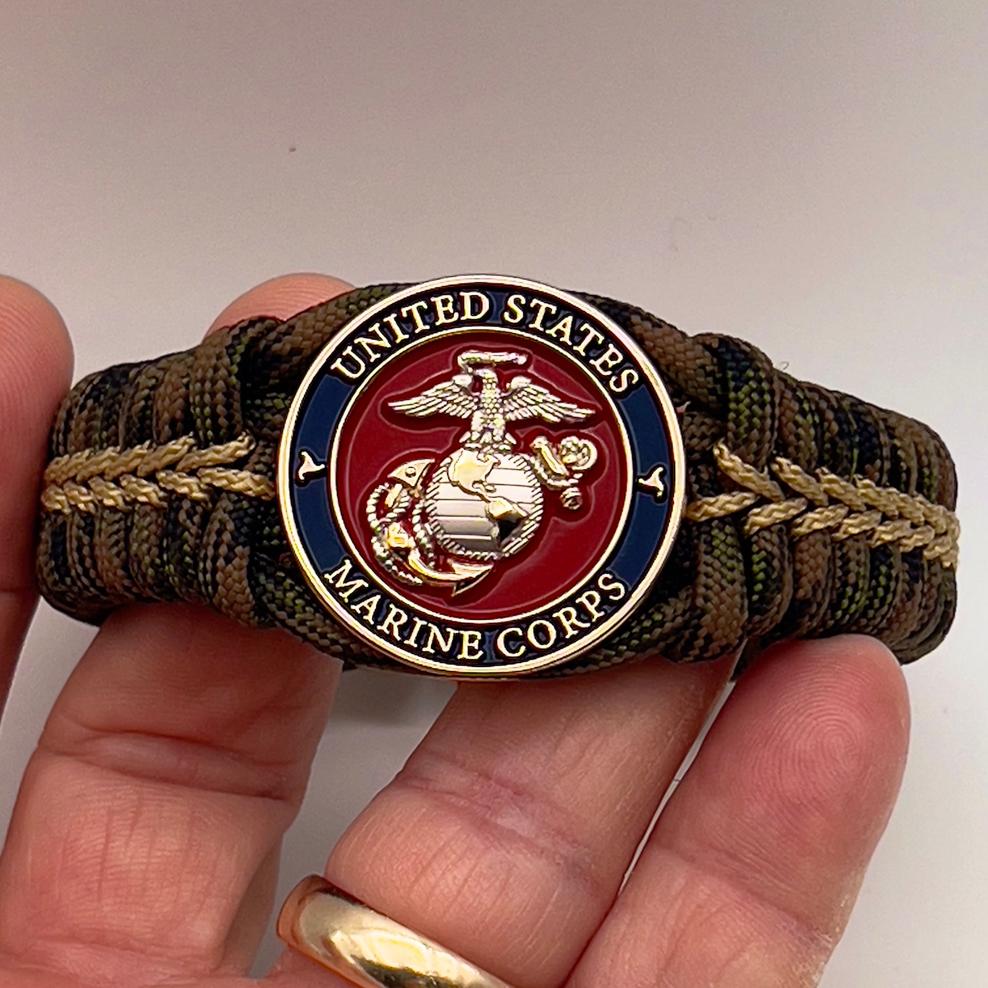 Thick, semi-rigid and comfortable braided United States Marine Corps bracelet featuring a 24K gold and silver plated USMC officer Eagle Globe and Anchor medallion, a gold Cobra style tactical buckle and woven with Woodland Camo 550 paracord and gold micro cord.