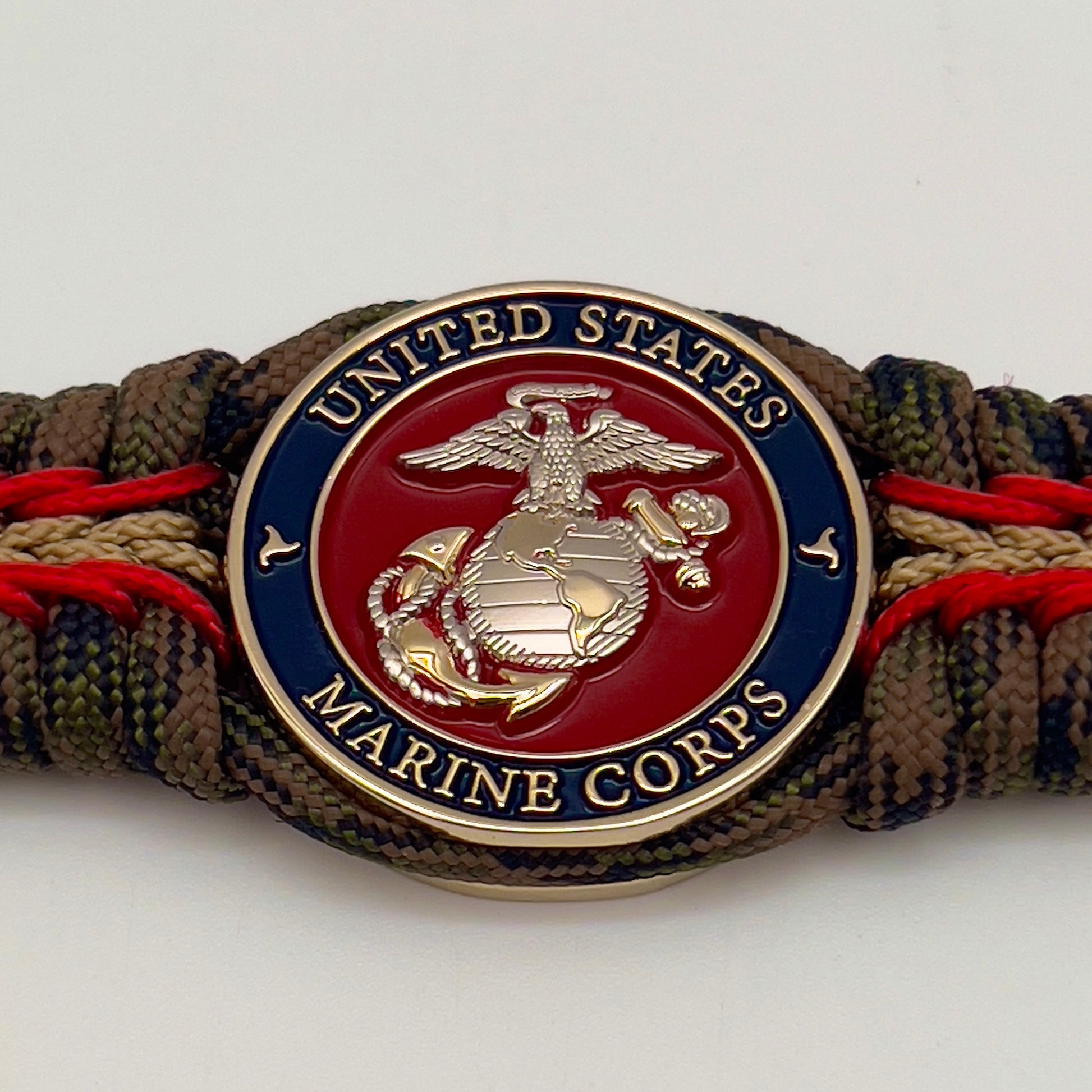 Thick, semi-rigid and comfortable braided United States Marine Corps bracelet featuring a 24K gold and silver plated USMC officer Eagle Globe and Anchor medallion, a gold Cobra style tactical buckle and woven with Woodland Camo 550 paracord and Imperial Red and gold micro cord.