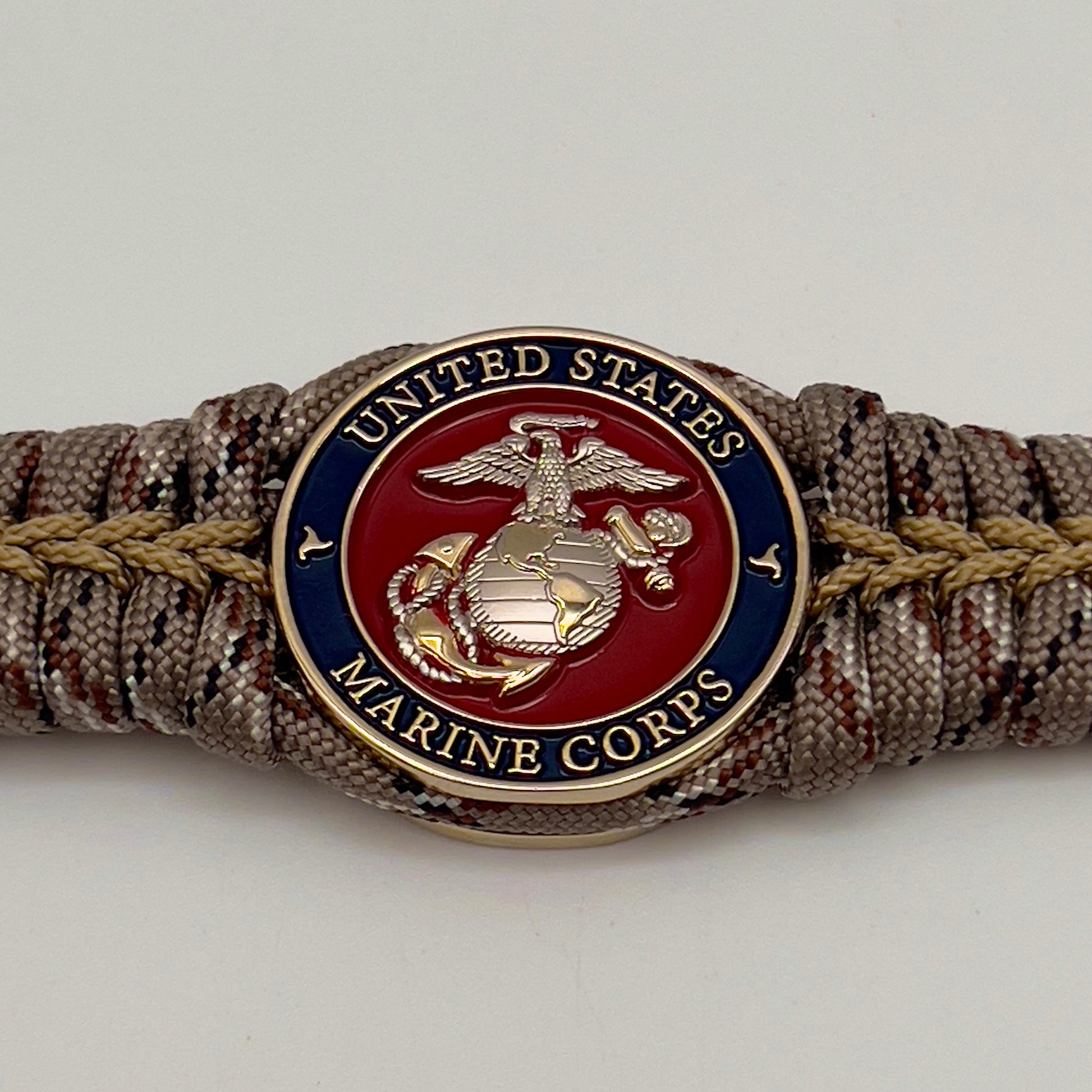 Thick and comfortable braided United States Marine Corps bracelet featuring a 24K gold and silver plated USMC officer Eagle Globe and Anchor medallion, a Cobra style tactical buckle and woven with Desert Camo 550 paracord gold micro cord.