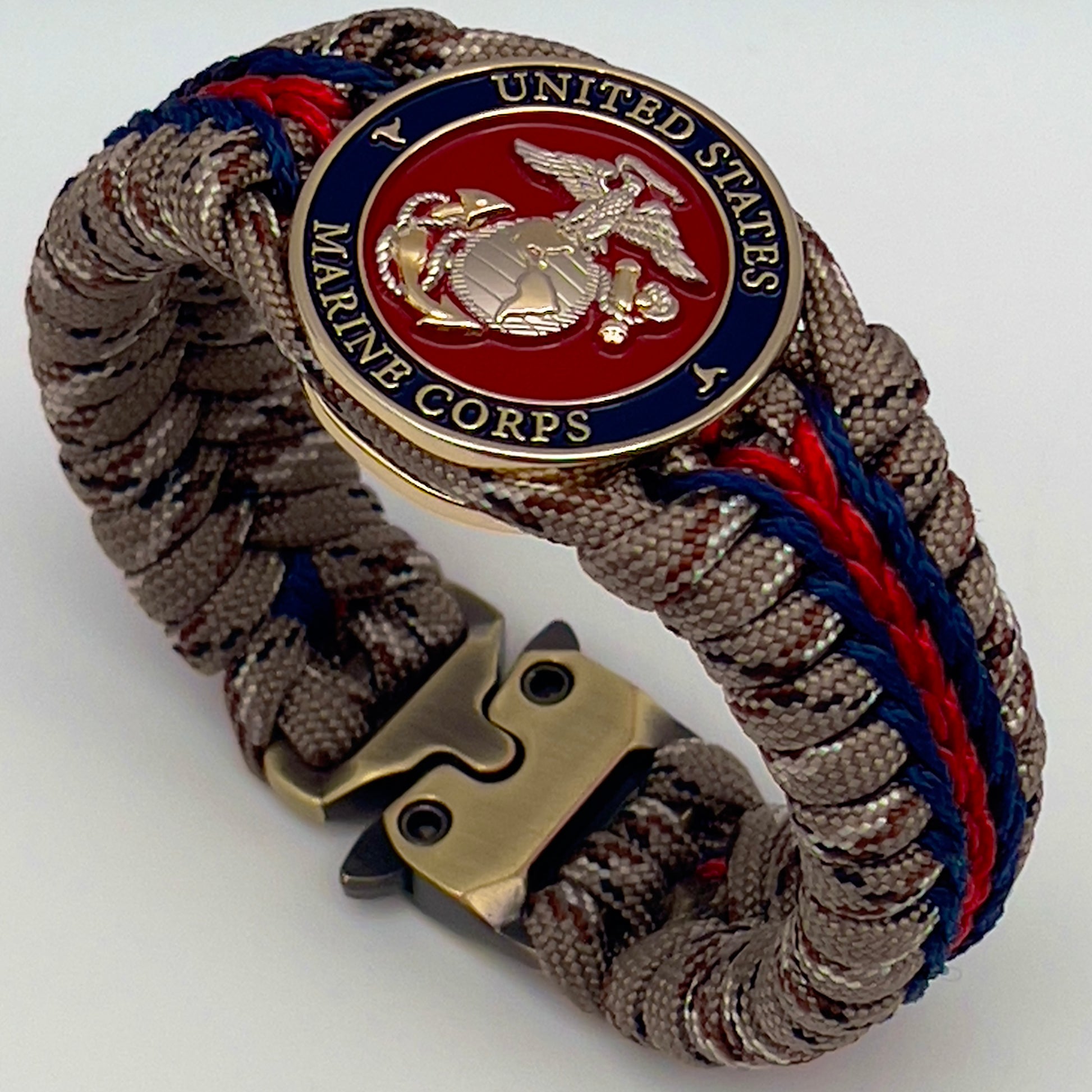 Thick and comfortable braided United States Marine Corps bracelet featuring a 24K gold and silver plated USMC officer Eagle Globe and Anchor medallion, a Cobra style tactical buckle and woven with Desert Camo 550 paracord and Imperial red and Navy Blue micro cord.
