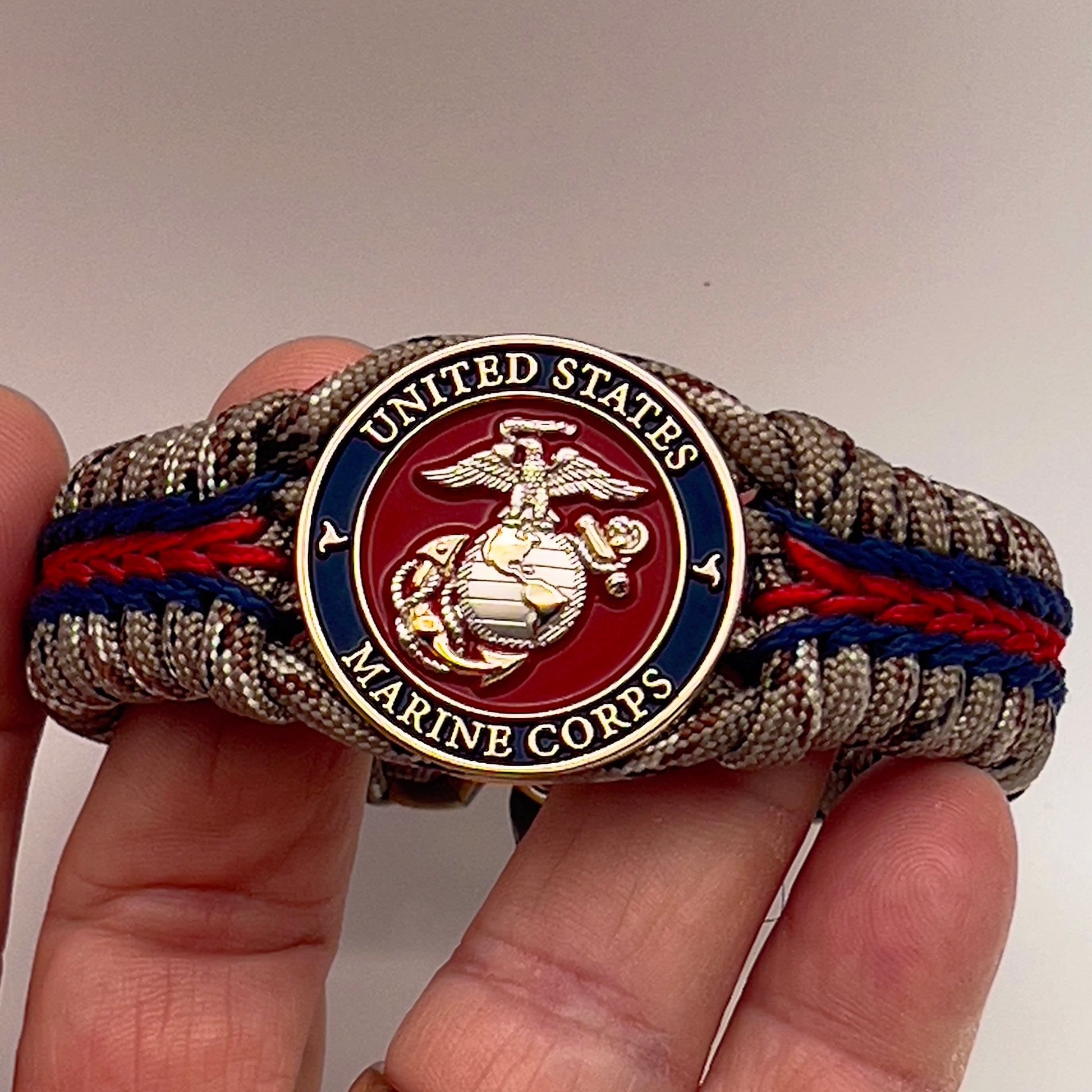 Thick and comfortable braided United States Marine Corps bracelet featuring a 24K gold and silver plated USMC officer Eagle Globe and Anchor medallion, a Cobra style tactical buckle and woven with Desert Camo 550 paracord and Imperial red and Navy Blue micro cord.