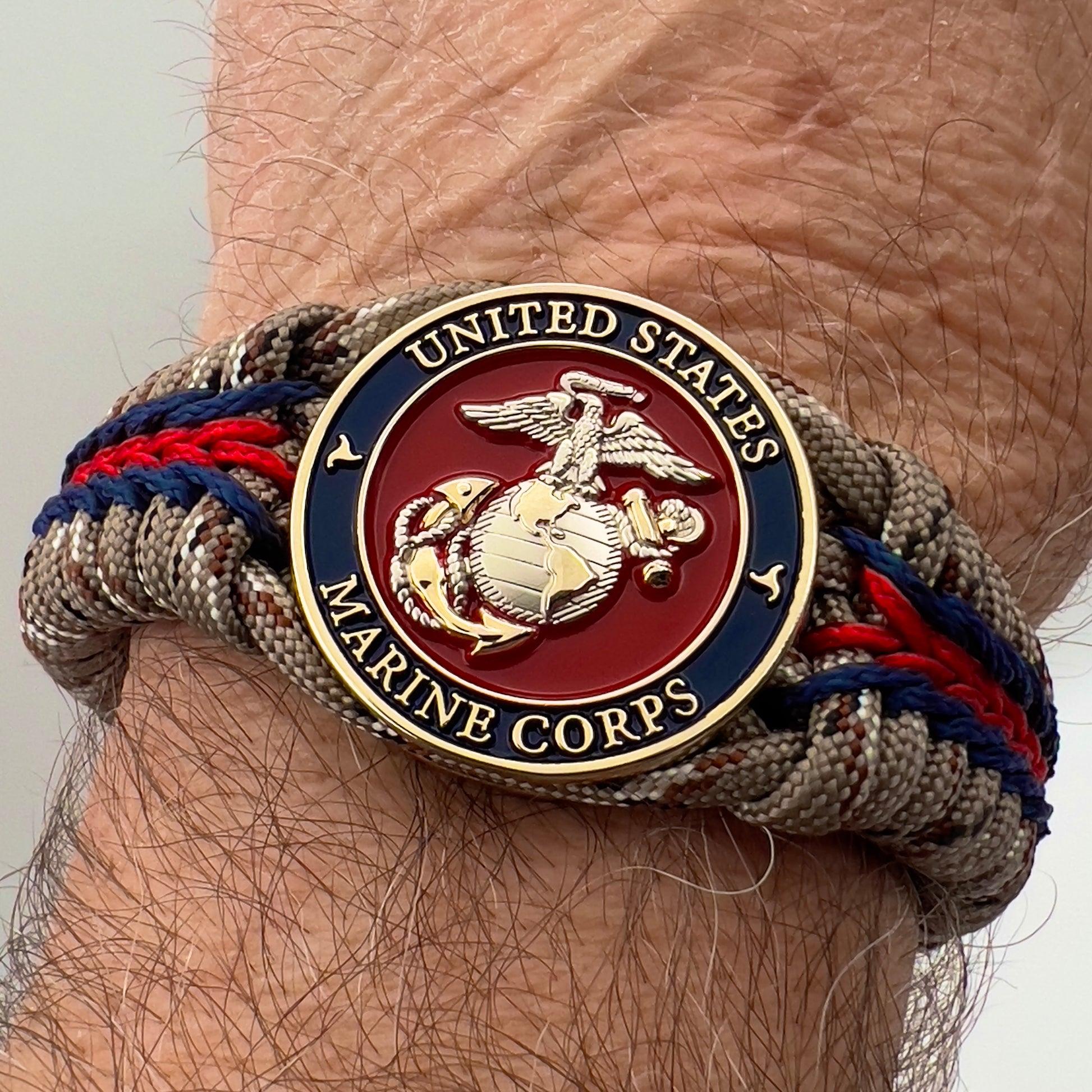 Thick and comfortable braided United States Marine Corps bracelet featuring a 24K gold and silver plated USMC officer Eagle Globe and Anchor medallion, a Cobra style tactical buckle and woven with Desert Camo 550 paracord and Imperial red and Navy Blue micro cord.