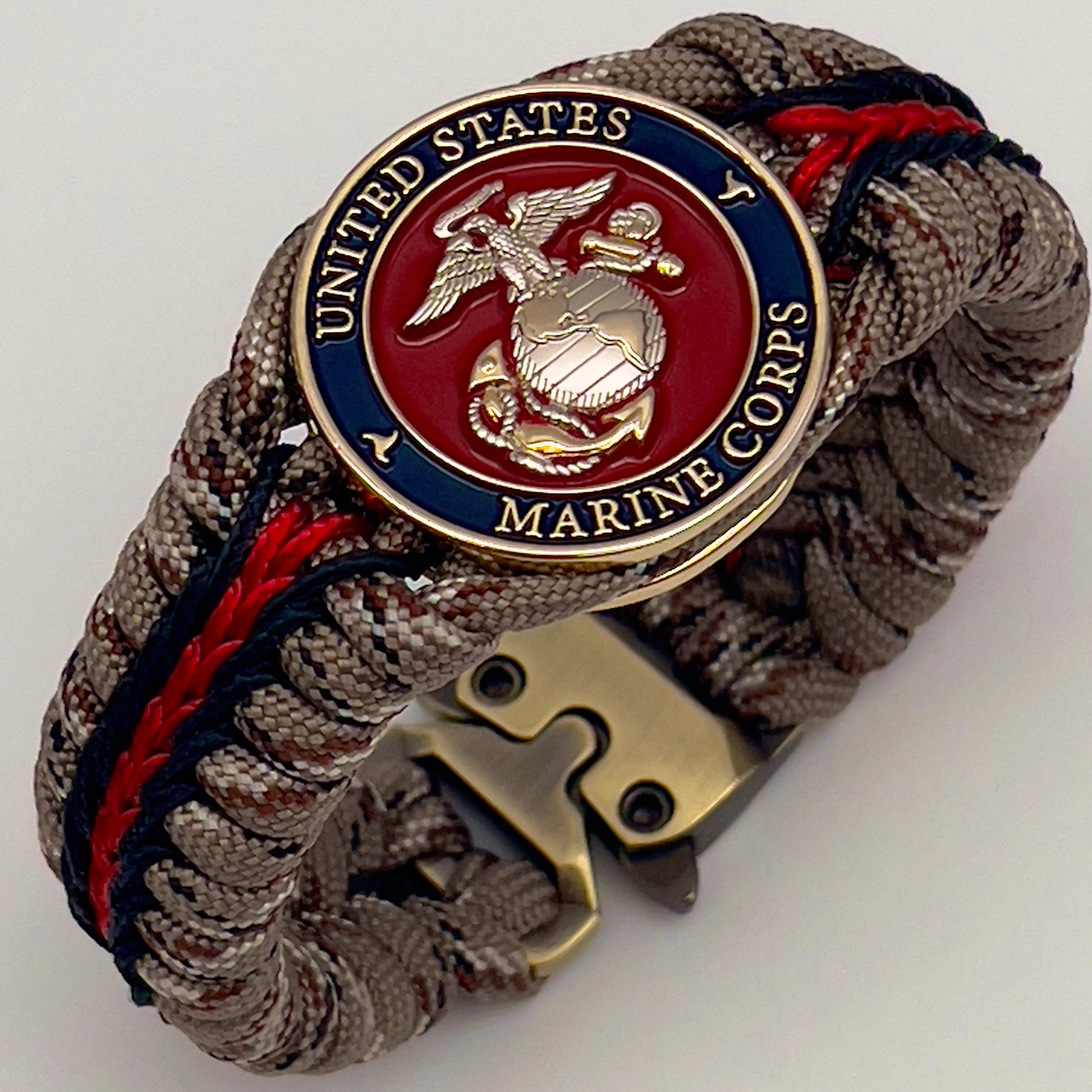 Thick and comfortable braided United States Marine Corps bracelet featuring a 24K gold and silver plated USMC officer Eagle Globe and Anchor medallion, a Cobra style tactical buckle and woven with Desert Camo 550 paracord and Imperial red and black micro cord.