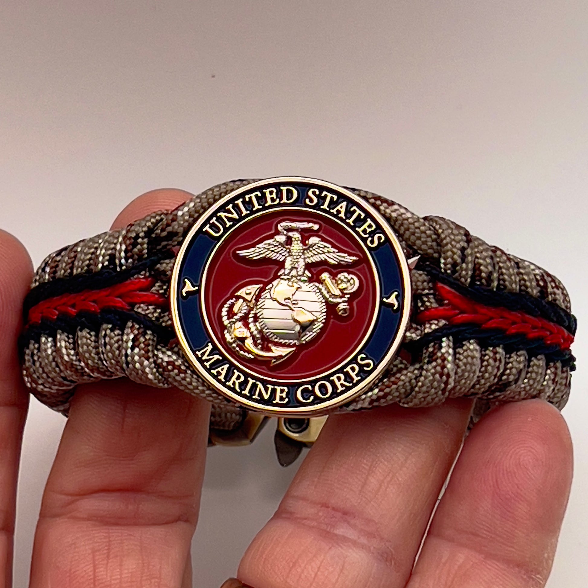 Thick and comfortable braided United States Marine Corps bracelet featuring a 24K gold and silver plated USMC officer Eagle Globe and Anchor medallion, a Cobra style tactical buckle and woven with Desert Camo 550 paracord and Imperial red and black micro cord.