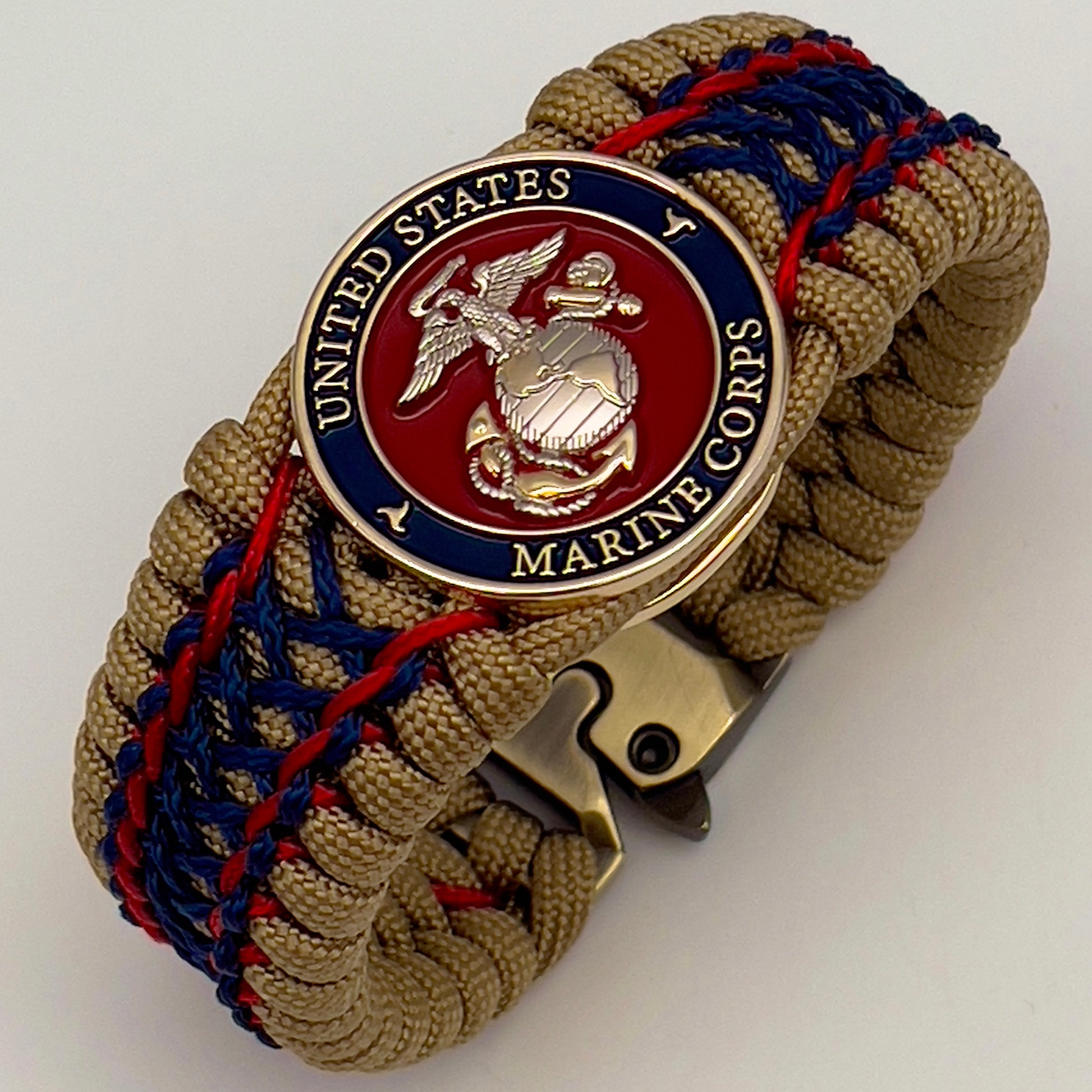 Thick and comfortable braided United States Marine Corps bracelet featuring a 24K gold and silver plated USMC officer Eagle Globe and Anchor medallion, a gold Cobra style tactical buckle and woven with gold 550 paracord and Imperial Red and Navy Blue micro cord.