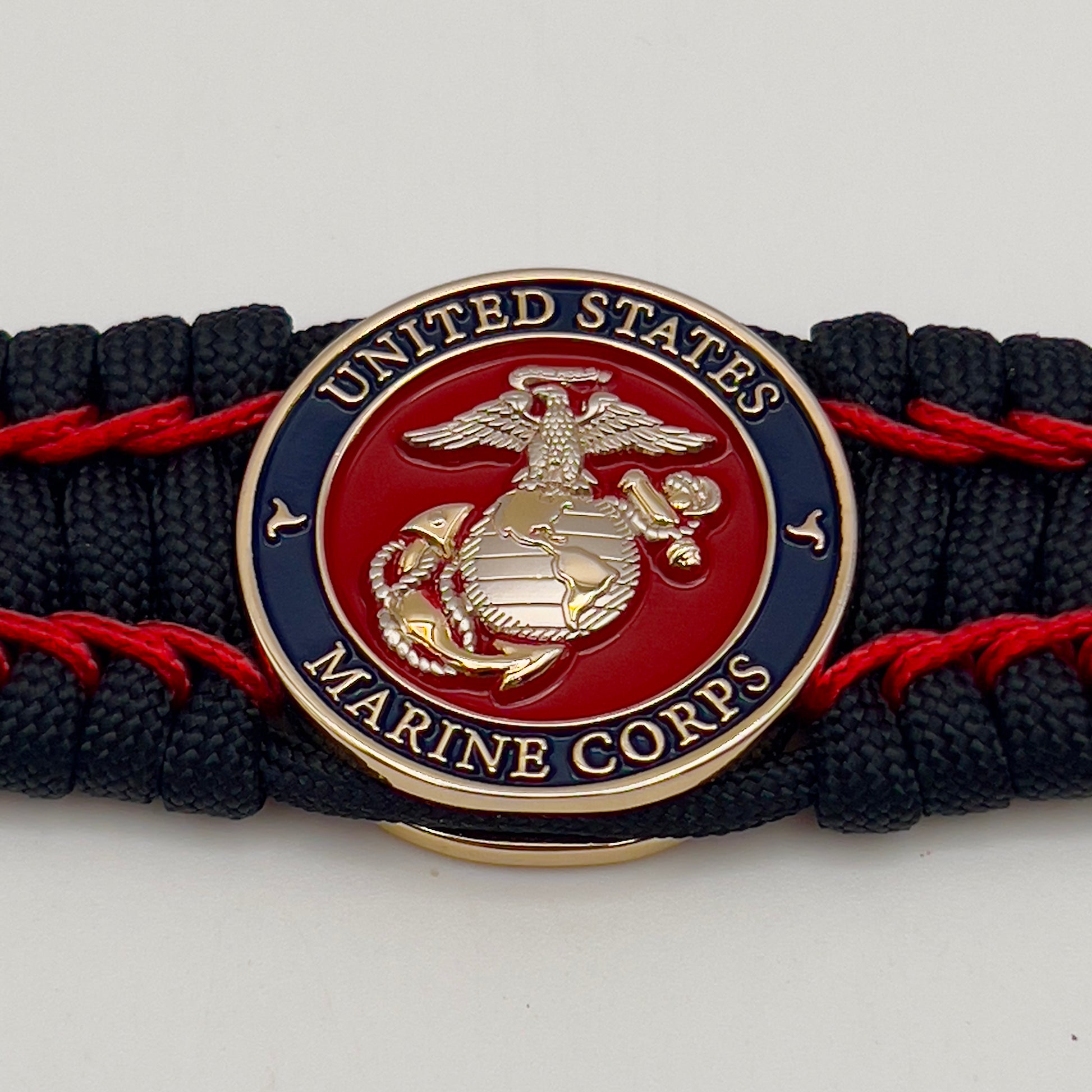 Thick and comfortable braided United States Marine Corps bracelet featuring a 24K gold and silver plated USMC officer Eagle Globe and Anchor medallion, a black Cobra style tactical buckle and woven with black 550 paracord and Imperial Red micro cord.