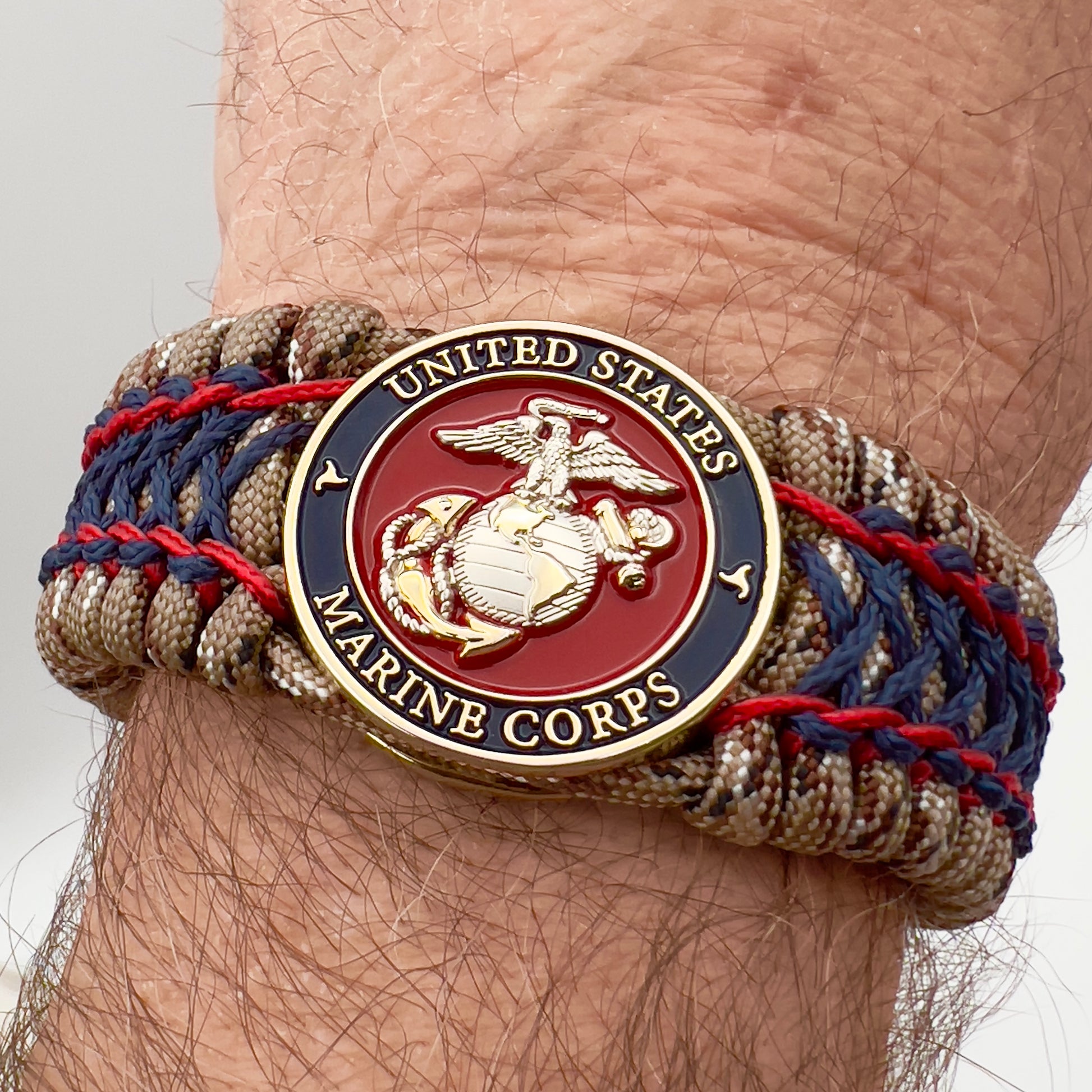 Thick and comfortable braided United States Marine Corps bracelet featuring a 24K gold and silver plated USMC officer Eagle Globe and Anchor medallion, a gold Cobra style tactical buckle and woven with Desert Camo 550 paracord and Imperial Red and Navy Blue micro cord.