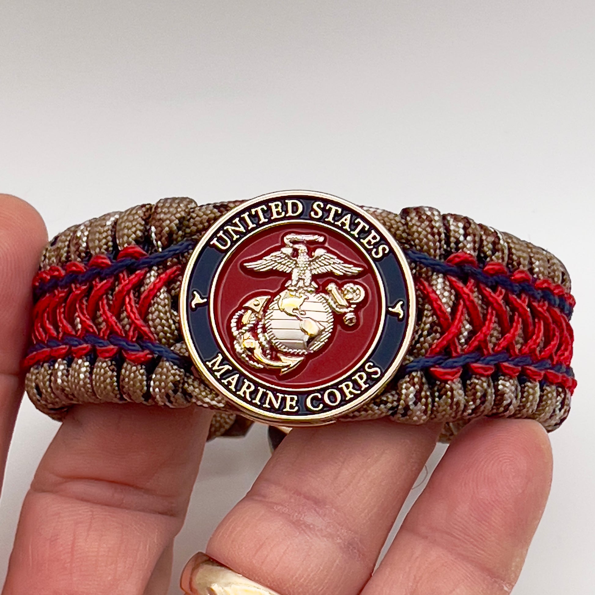 Thick and comfortable braided United States Marine Corps bracelet featuring a 24K gold and silver plated USMC officer Eagle Globe and Anchor medallion, a gold Cobra style tactical buckle and woven with Desert Camo 550 paracord and Imperial Red and Navy Blue micro cord.