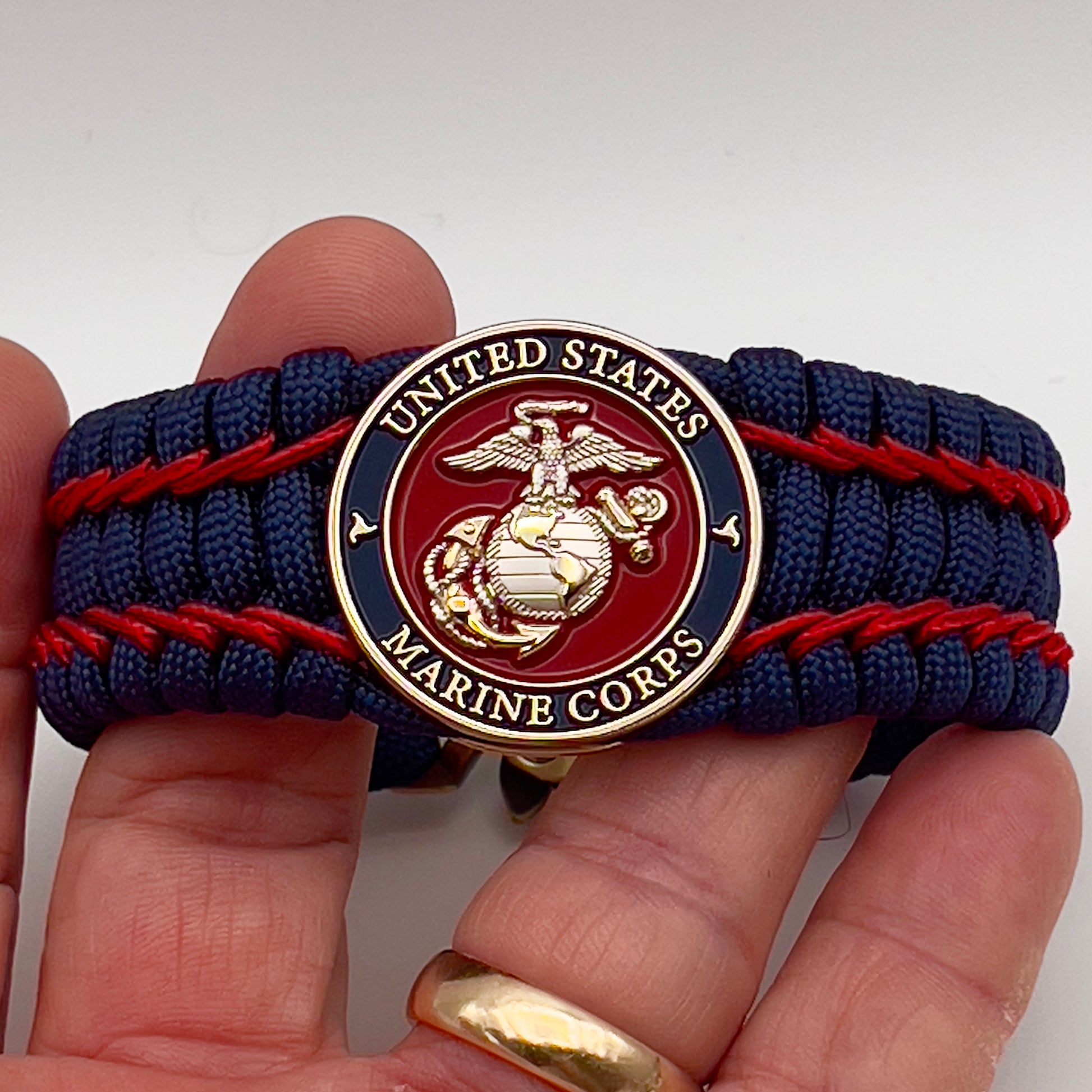 Thick and comfortable braided United States Marine Corps bracelet featuring a 24K gold and silver plated USMC officer Eagle Globe and Anchor medallion, a Cobra style tactical buckle and woven with gold 550 paracord and Imperial Red micro cord.