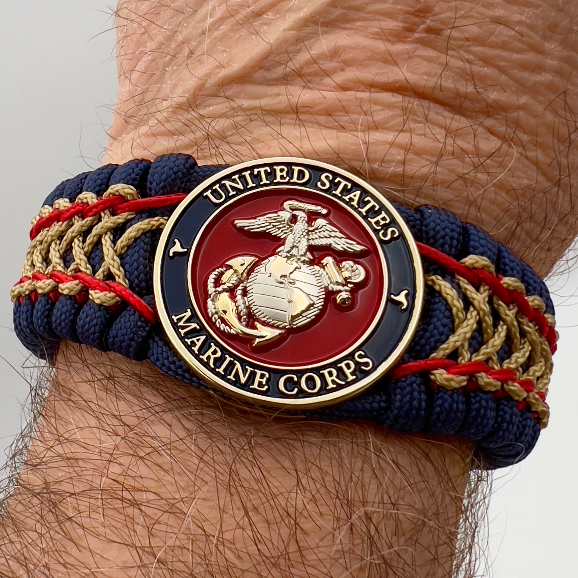Thick and comfortable braided United States Marine Corps bracelet featuring a 24K gold and silver plated USMC officer Eagle Globe and Anchor medallion, a Cobra style tactical buckle and woven with gold 550 paracord and Imperial Red and Gold micro cord.