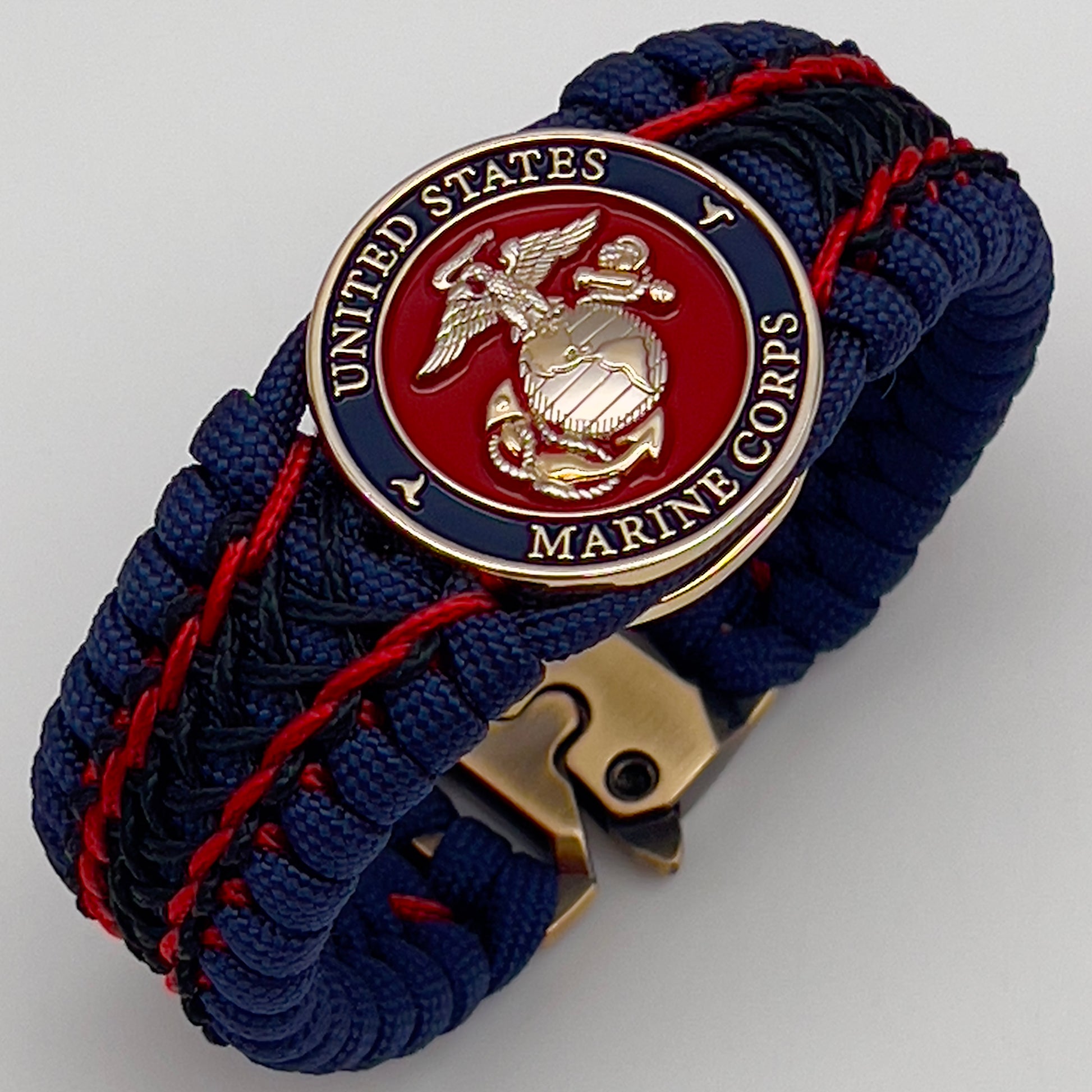 Thick and comfortable braided United States Marine Corps bracelet featuring a 24K gold and silver plated USMC officer Eagle Globe and Anchor medallion, a Cobra style tactical buckle and woven with gold 550 paracord and Imperial Red and Black micro cord.