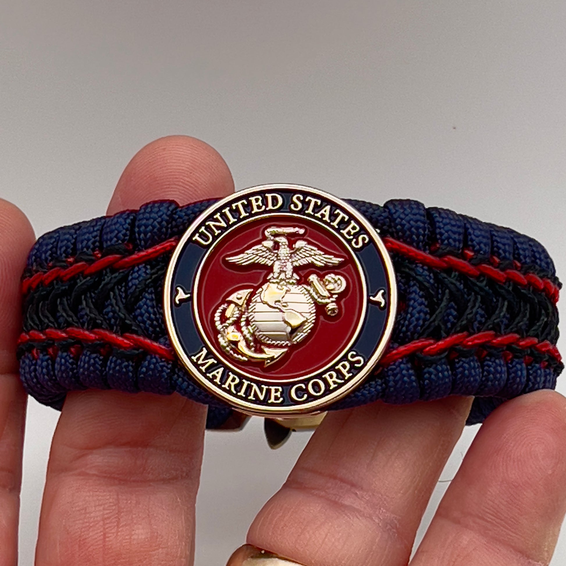 Thick and comfortable braided United States Marine Corps bracelet featuring a 24K gold and silver plated USMC officer Eagle Globe and Anchor medallion, a Cobra style tactical buckle and woven with gold 550 paracord and Imperial Red and Black micro cord.