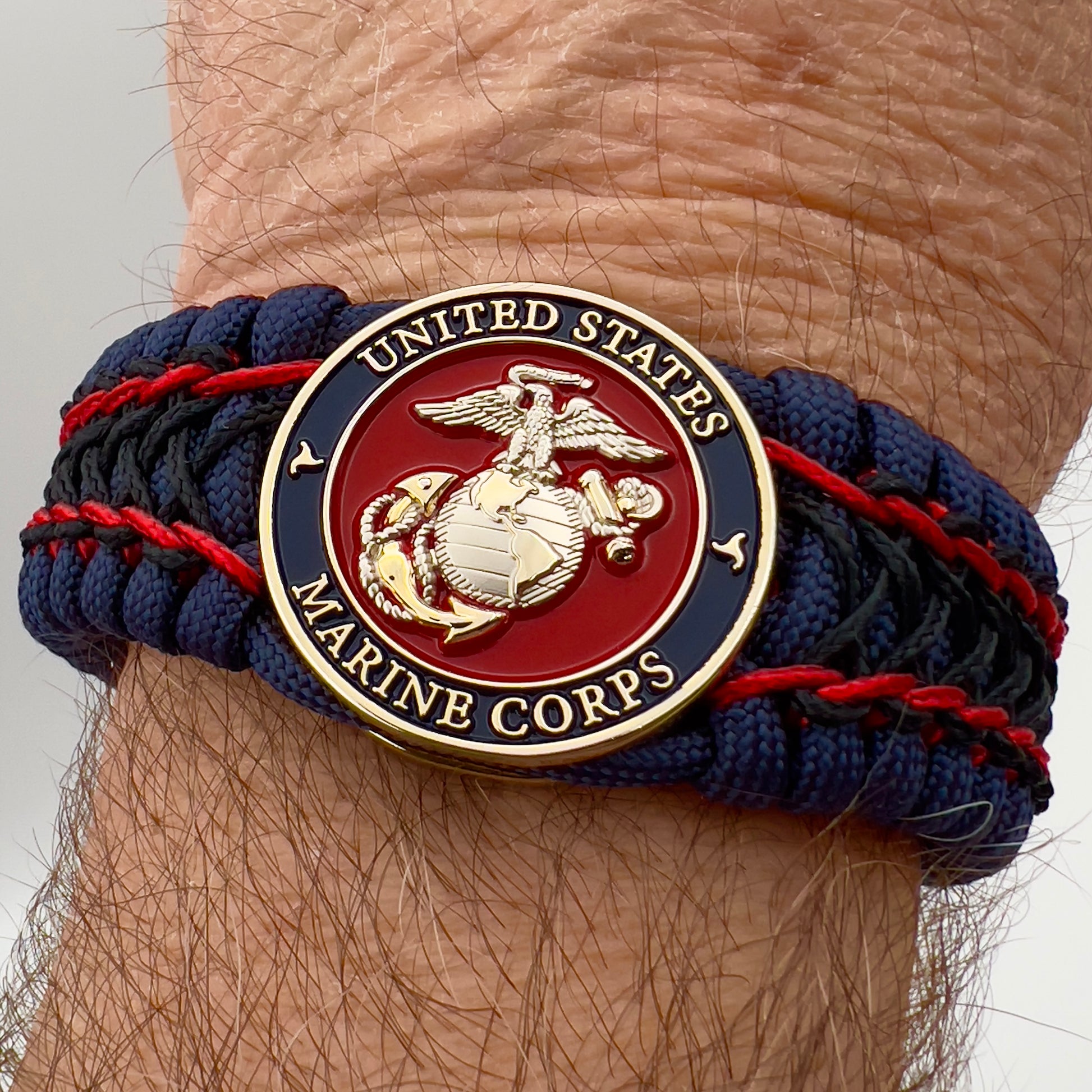 Thick and comfortable braided United States Marine Corps bracelet featuring a 24K gold and silver plated USMC officer Eagle Globe and Anchor medallion, a Cobra style tactical buckle and woven with gold 550 paracord and Imperial Red and Black micro cord.