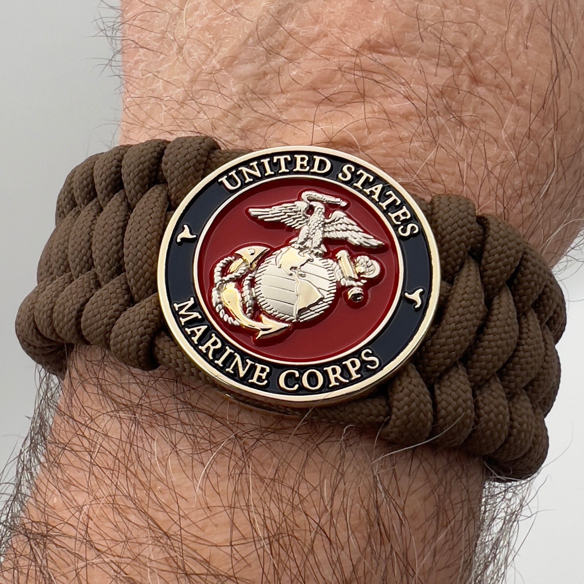 Thick and comfortable braided United States Marine Corps bracelet featuring a 24K gold and silver plated USMC officer Eagle Globe and Anchor medallion, a Cobra style tactical buckle and woven with Coyote Brown 550 paracord.