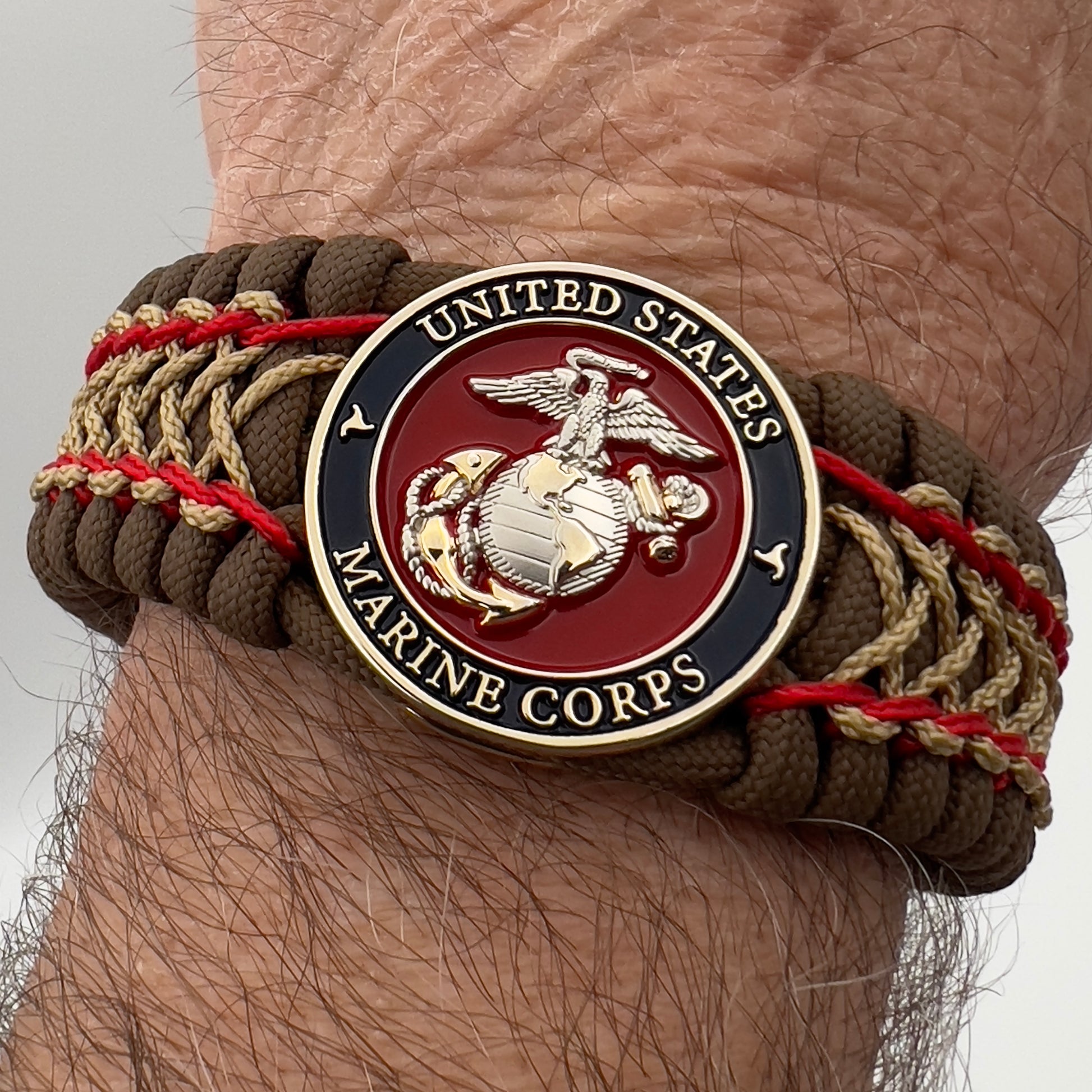 Thick and comfortable braided United States Marine Corps bracelet featuring a 24K gold and silver plated USMC officer Eagle Globe and Anchor medallion, a Cobra style tactical buckle and woven with Coyote Brown 550 paracord and Imperial Red and gold micro cord.