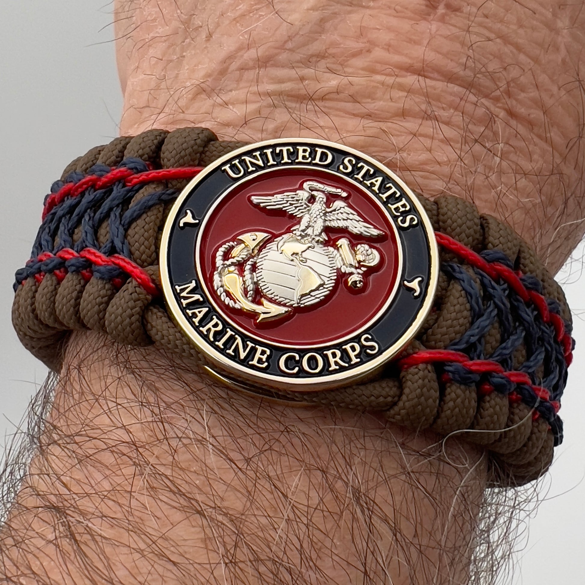 Thick and comfortable braided United States Marine Corps bracelet featuring a 24K gold and silver plated USMC officer Eagle Globe and Anchor medallion, a Cobra style tactical buckle and woven with Coyote Brown 550 paracord and Imperial Red and Navy Blue micro cord.
