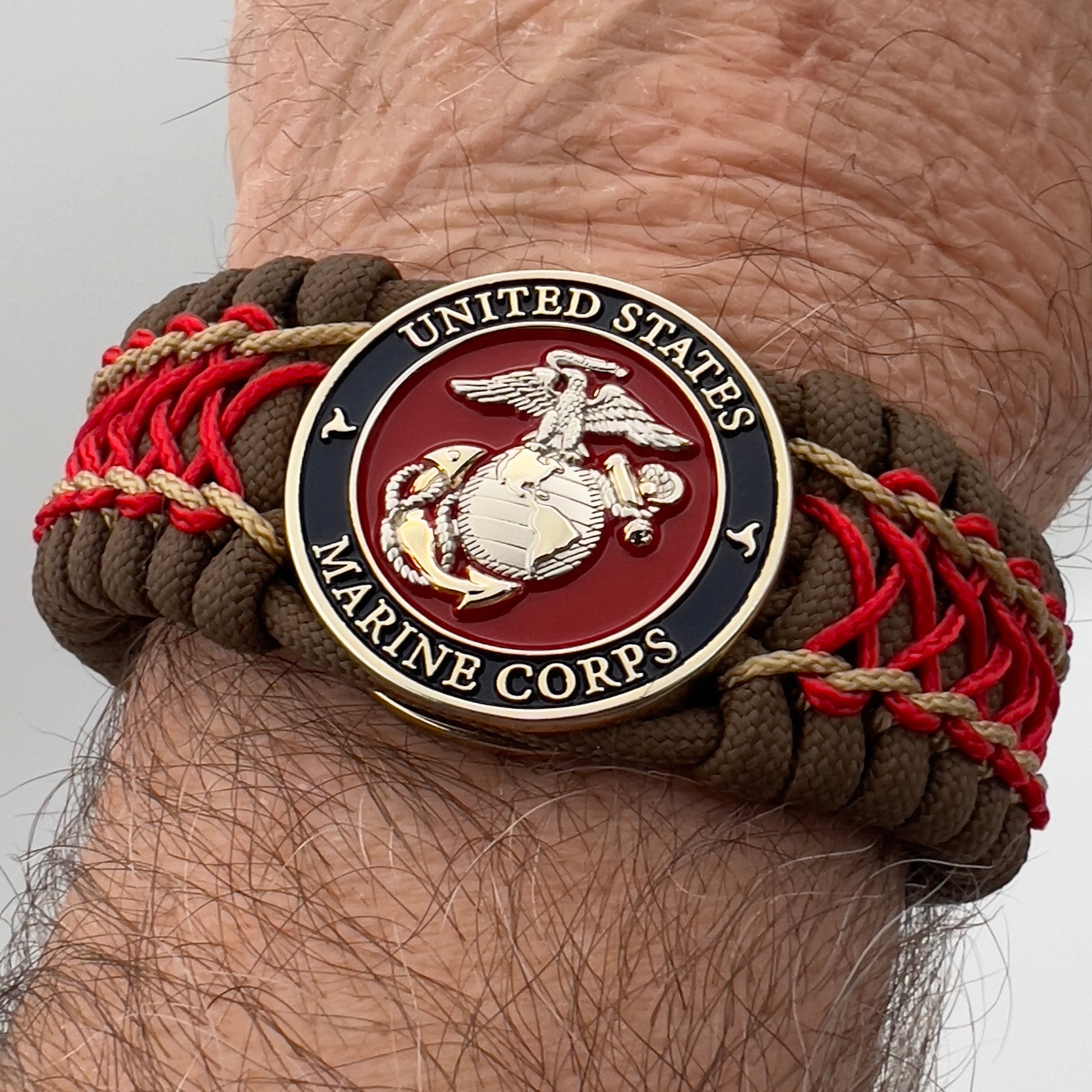 Thick and comfortable braided United States Marine Corps bracelet featuring a 24K gold and silver plated USMC officer Eagle Globe and Anchor medallion, a Cobra style tactical buckle and woven with Coyote Brown 550 paracord and Imperial Red and gold micro cord.