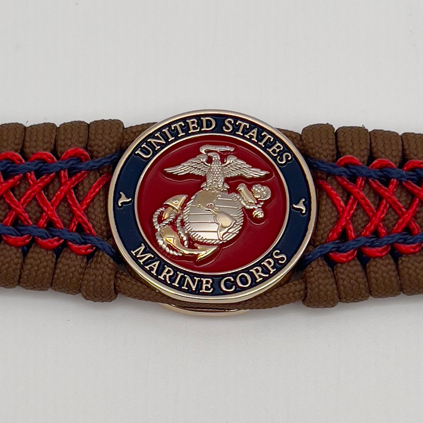 Thick and comfortable braided United States Marine Corps bracelet featuring a 24K gold and silver plated USMC officer Eagle Globe and Anchor medallion, a Cobra style tactical buckle and woven with Coyote Brown 550 paracord and Imperial Red and Navy Blue micro cord.