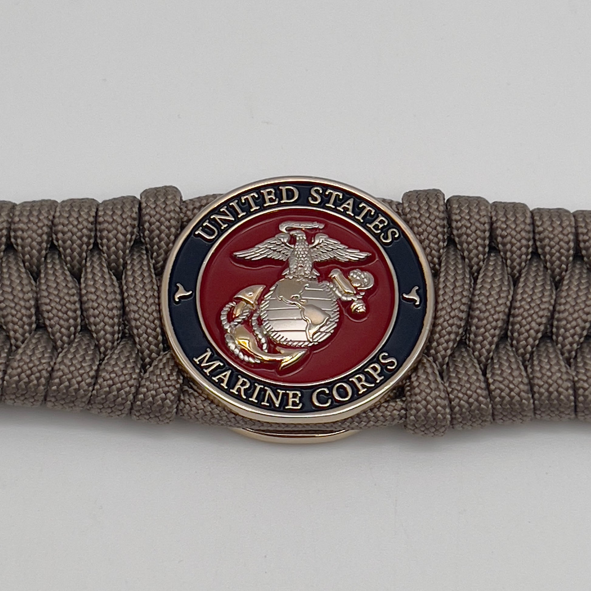 Thick and comfortable braided United States Marine Corps bracelet featuring a 24K gold and silver plated USMC officer Eagle Globe and Anchor medallion, a Cobra style tactical buckle and woven with tan 550 paracord.