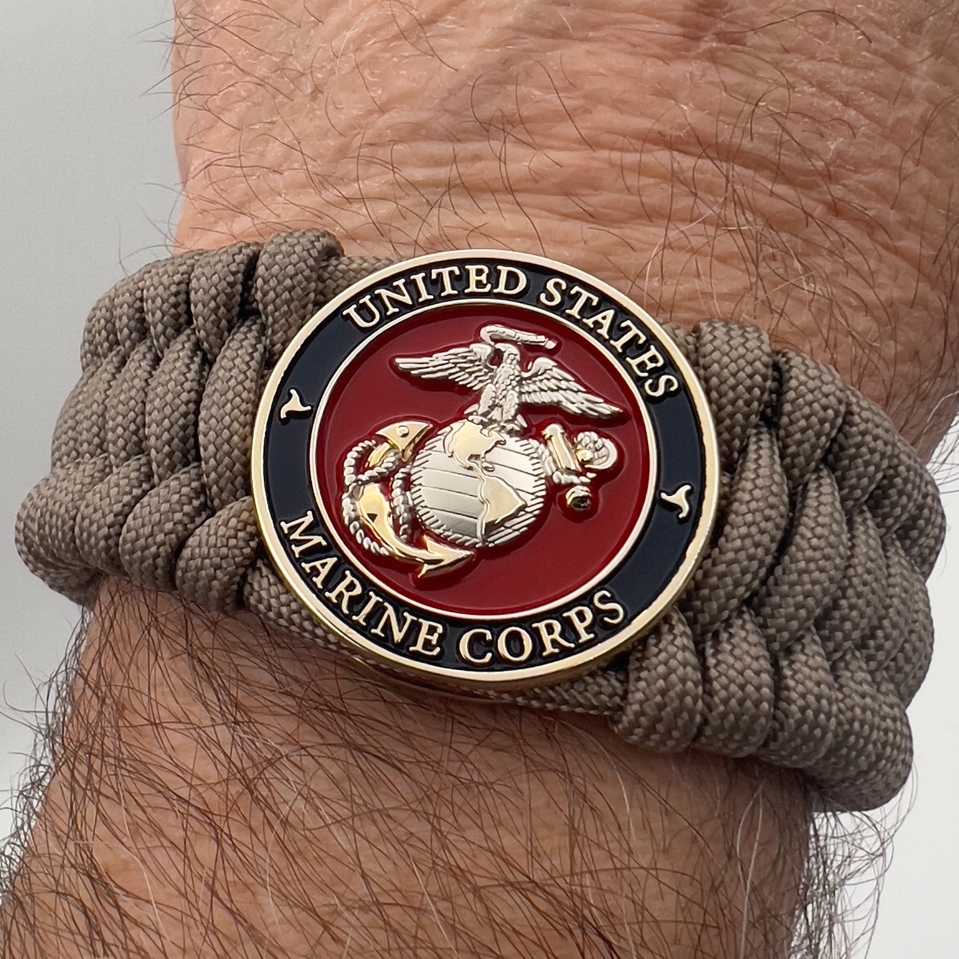 Thick and comfortable braided United States Marine Corps bracelet featuring a 24K gold and silver plated USMC officer Eagle Globe and Anchor medallion, a Cobra style tactical buckle and woven with tan 550 paracord.