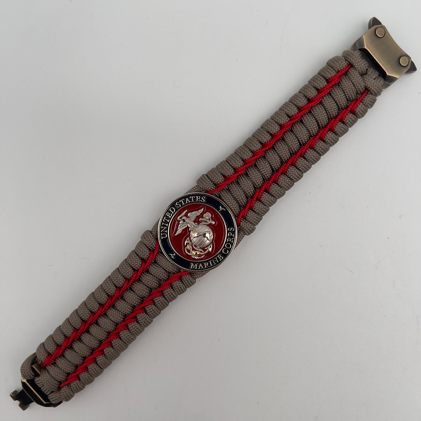 Thick, semi-rigid and comfortable braided United States Marine Corps bracelet featuring a 24K gold and silver plated USMC officer Eagle Globe and Anchor medallion, a gold Cobra style tactical buckle and woven with tan 550 paracord and Imperial Red micro cord.