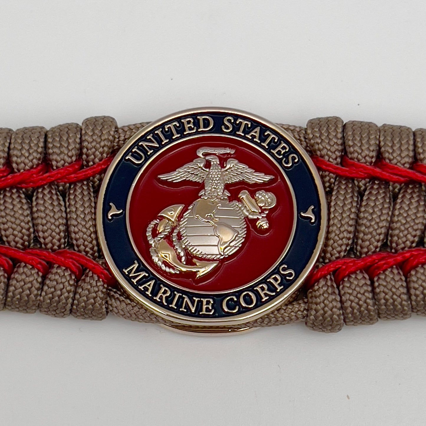 Thick, semi-rigid and comfortable braided United States Marine Corps bracelet featuring a 24K gold and silver plated USMC officer Eagle Globe and Anchor medallion, a gold Cobra style tactical buckle and woven with tan 550 paracord and Imperial Red micro cord.