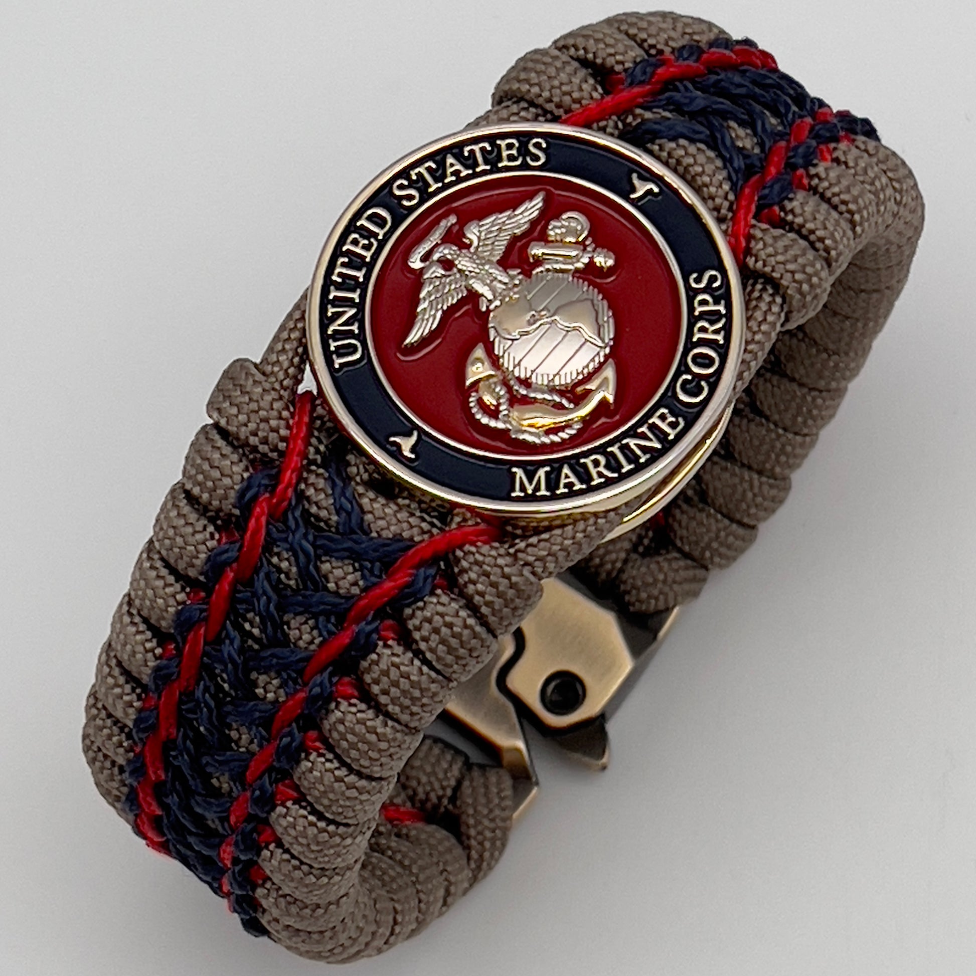 Thick, rigid and comfortable braided United States Marine Corps bracelet featuring a 24K gold and silver plated USMC officer Eagle Globe and Anchor medallion, a gold Cobra style tactical buckle and woven with tan 550 paracord and Imperial Red and Navy Blue micro cord.