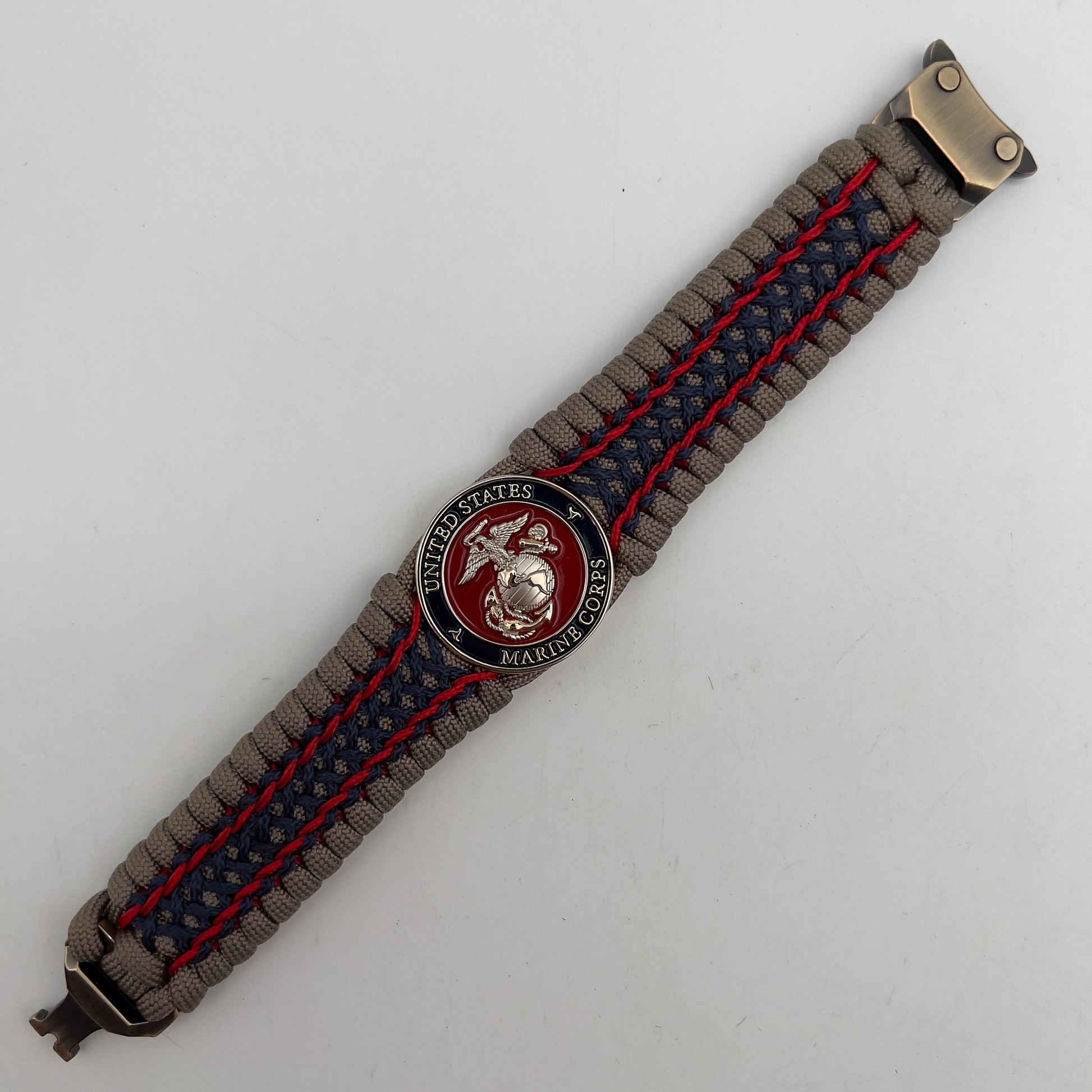 Thick, rigid and comfortable braided United States Marine Corps bracelet featuring a 24K gold and silver plated USMC officer Eagle Globe and Anchor medallion, a gold Cobra style tactical buckle and woven with tan 550 paracord and Imperial Red and Navy Blue micro cord.