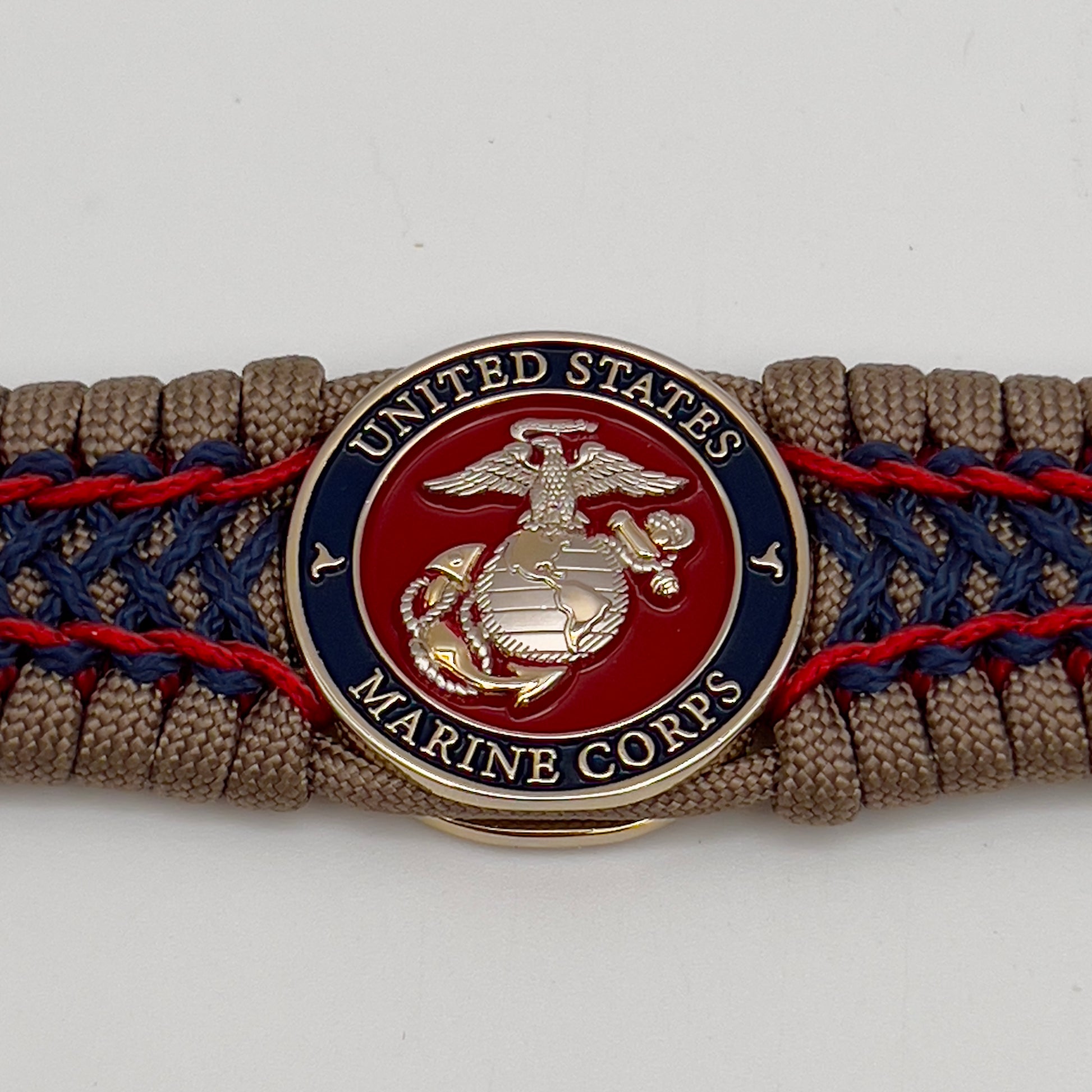 Thick, rigid and comfortable braided United States Marine Corps bracelet featuring a 24K gold and silver plated USMC officer Eagle Globe and Anchor medallion, a gold Cobra style tactical buckle and woven with tan 550 paracord and Imperial Red and Navy Blue micro cord.