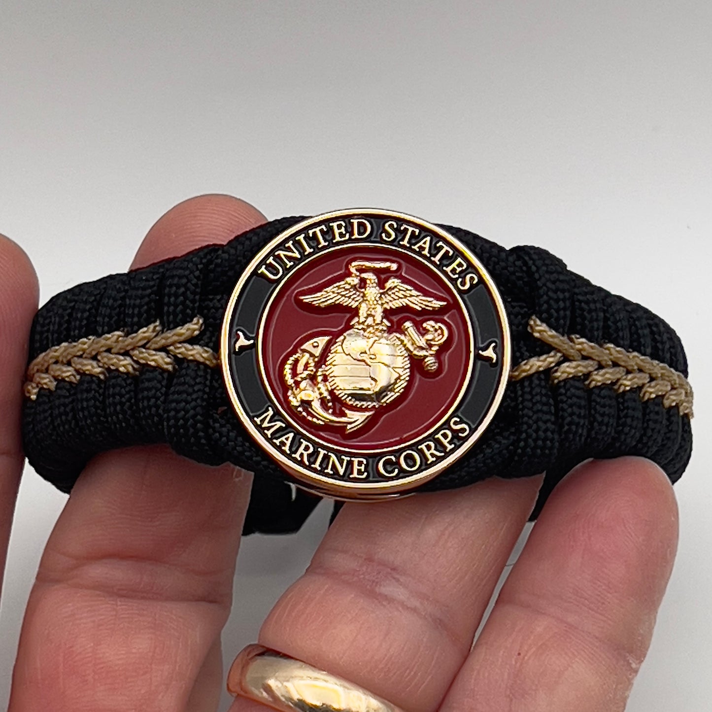 Thick, semi-rigid and comfortable braided United States Marine Corps bracelet featuring a 24K gold plated USMC officer Eagle Globe and Anchor medallion, a black Cobra style tactical buckle and woven with black 550 paracord and gold micro cord.