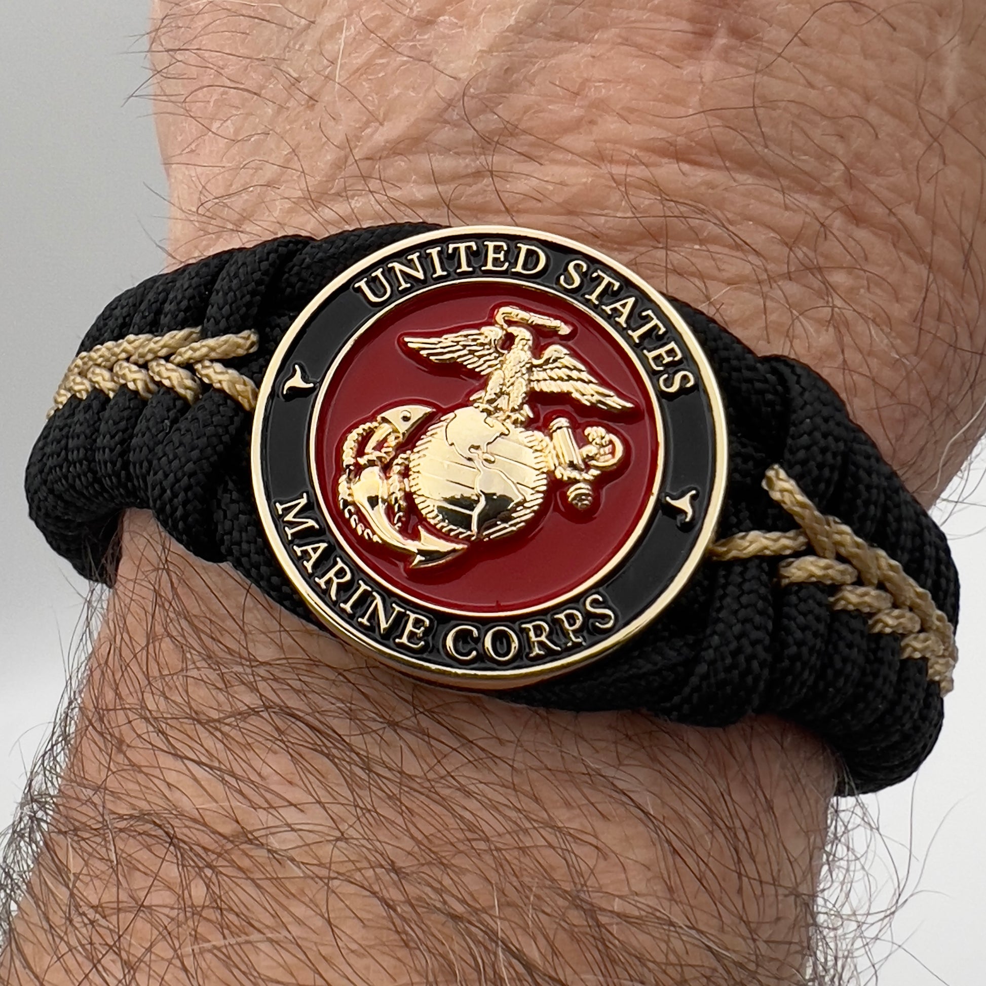 Thick, semi-rigid and comfortable braided United States Marine Corps bracelet featuring a 24K gold plated USMC officer Eagle Globe and Anchor medallion, a black Cobra style tactical buckle and woven with black 550 paracord and gold micro cord.