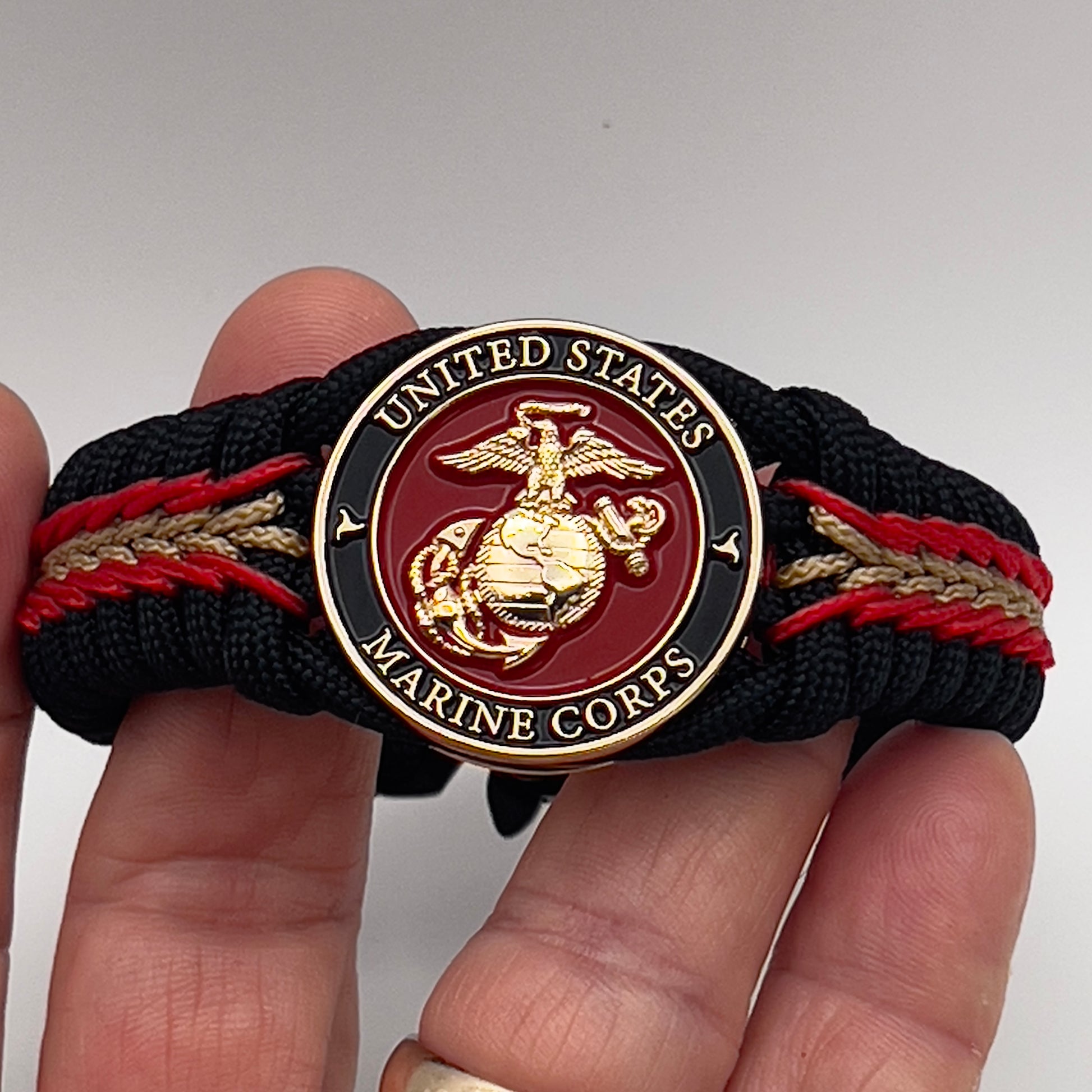 Thick, semi-rigid and comfortable braided United States Marine Corps bracelet featuring a 24K gold and silver plated USMC officer Eagle Globe and Anchor medallion, a black Cobra style tactical buckle and woven with black 550, Imperial red and gold micro paracord.